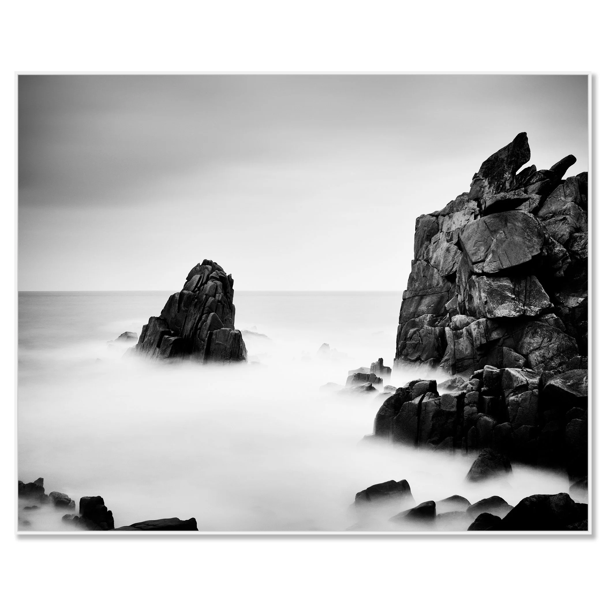 Black-and-white photograph of rocky sea cliffs and a lone sea stack in calm mist – framed ArtBox white