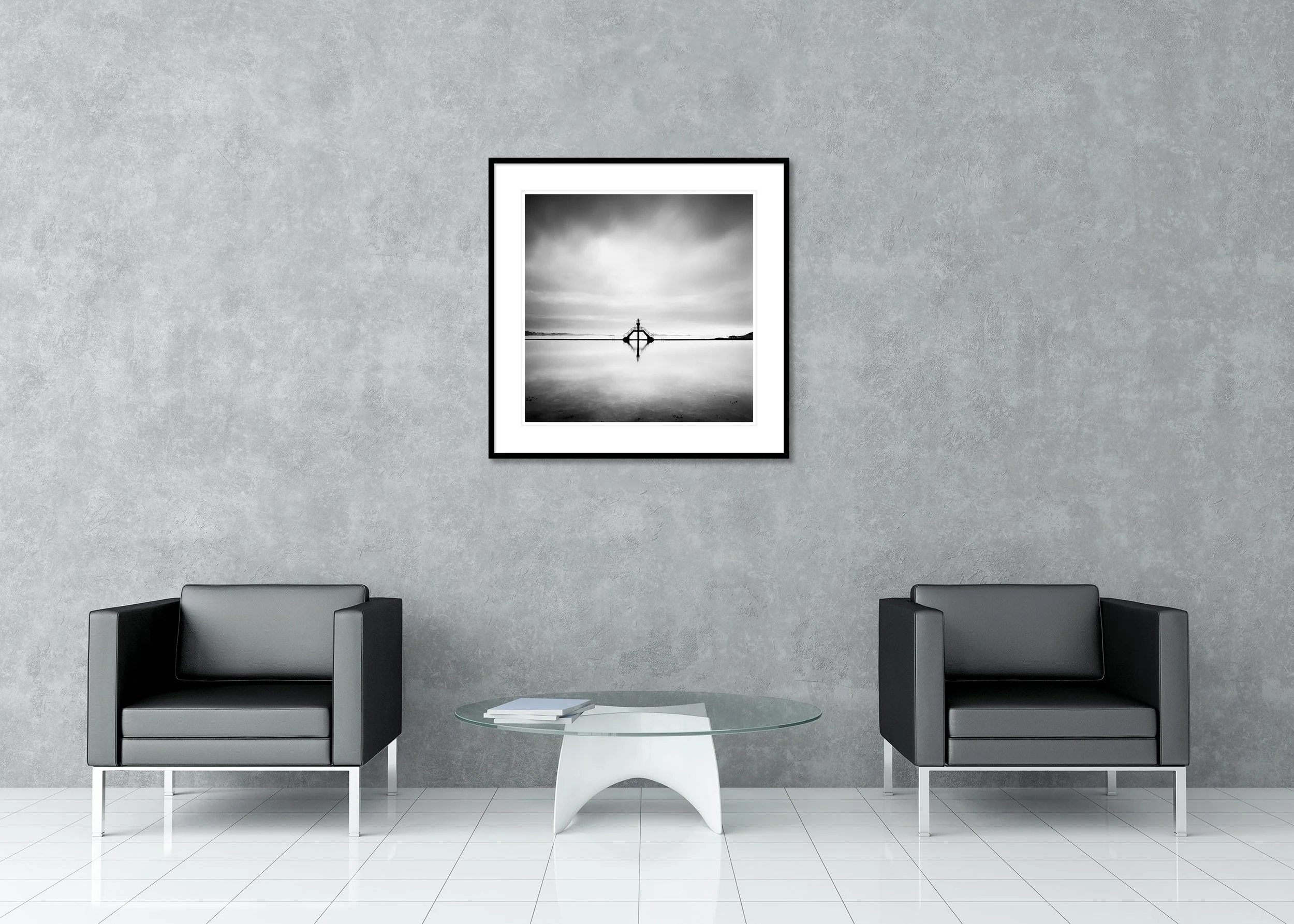 Black and white photograph of a minimalist seascape with a symmetrical diving platform reflected in calm, still water under a cloudy sky, presented as an archival pigment print in a classic frame with passe-partout.