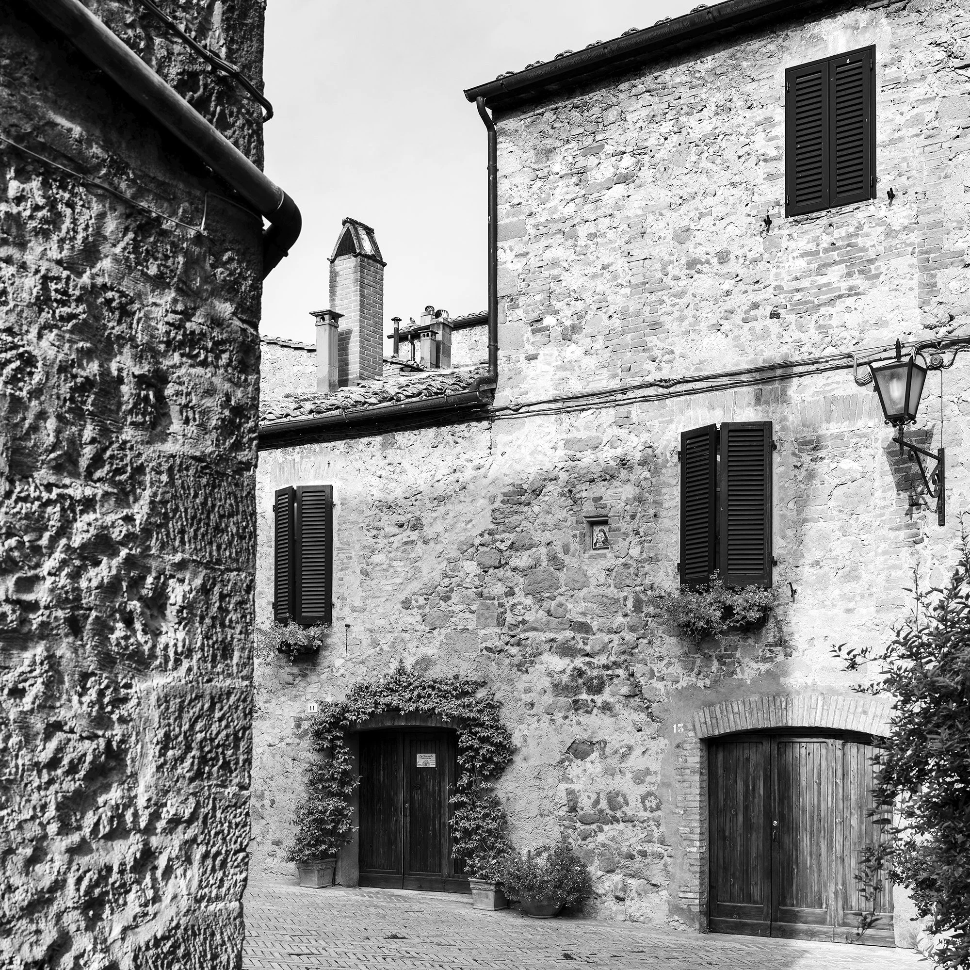 Gerald Berghammer - Black and white cityscape photography. Old stone building with wooden shutters, potted plants and outdoor seating in a narrow courtyard. Print detail 2