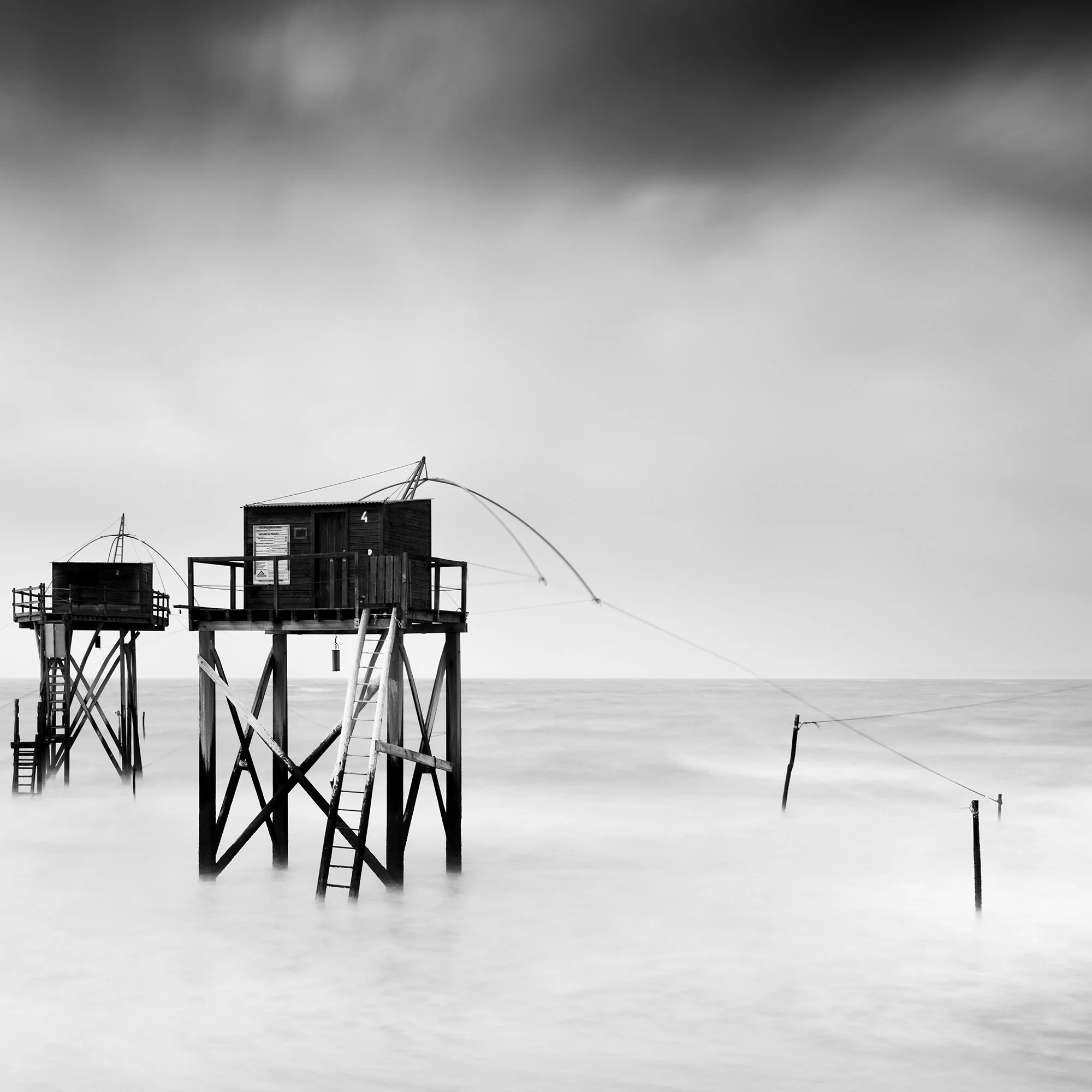 Monochrome long-exposure seascape with wooden fishing huts on stilts and misty water, Detail 2