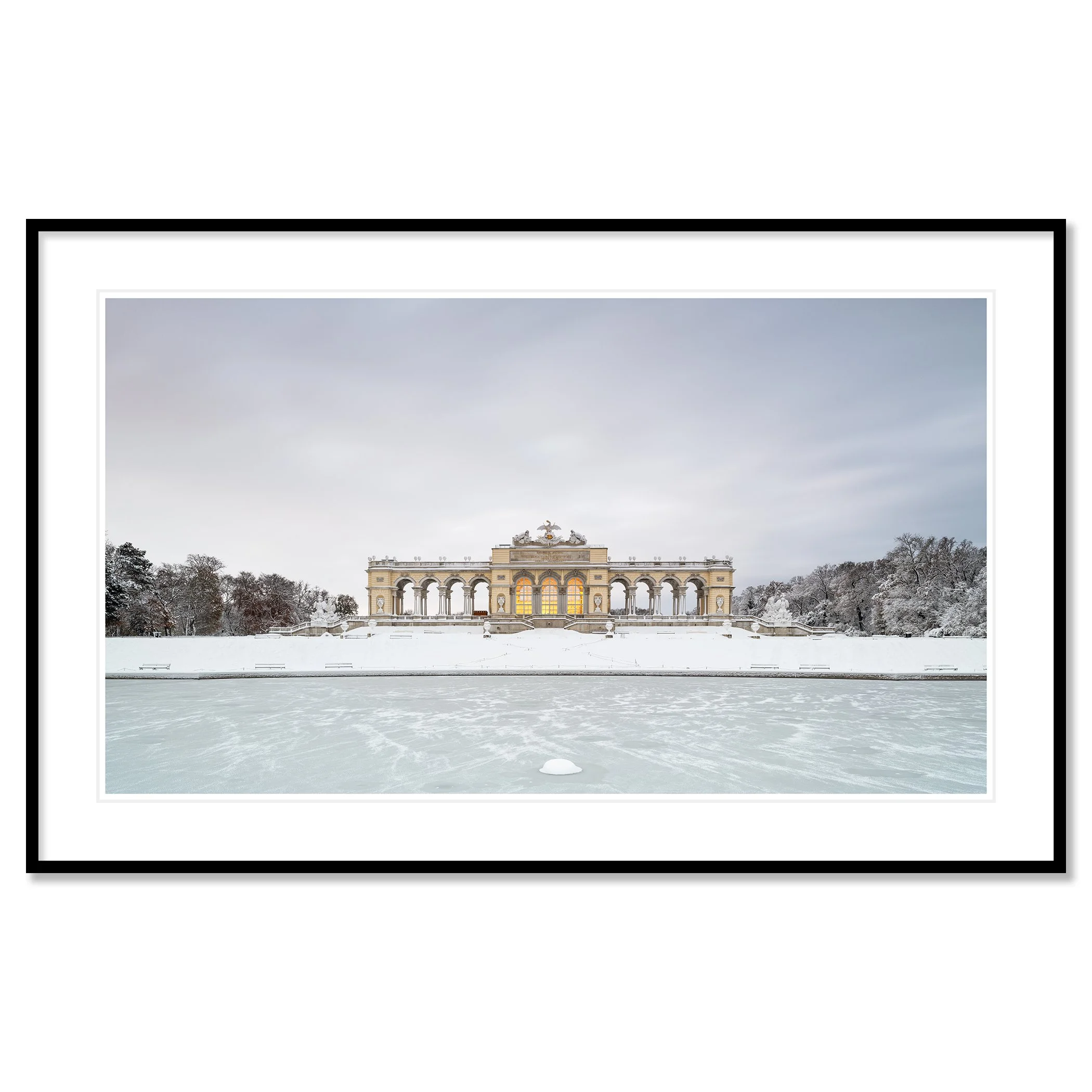 Gerald Berghammer - Color Photography. A historic building on a snow-covered landscape, surrounded by leafless trees, with a frozen body of water. Classic framed black