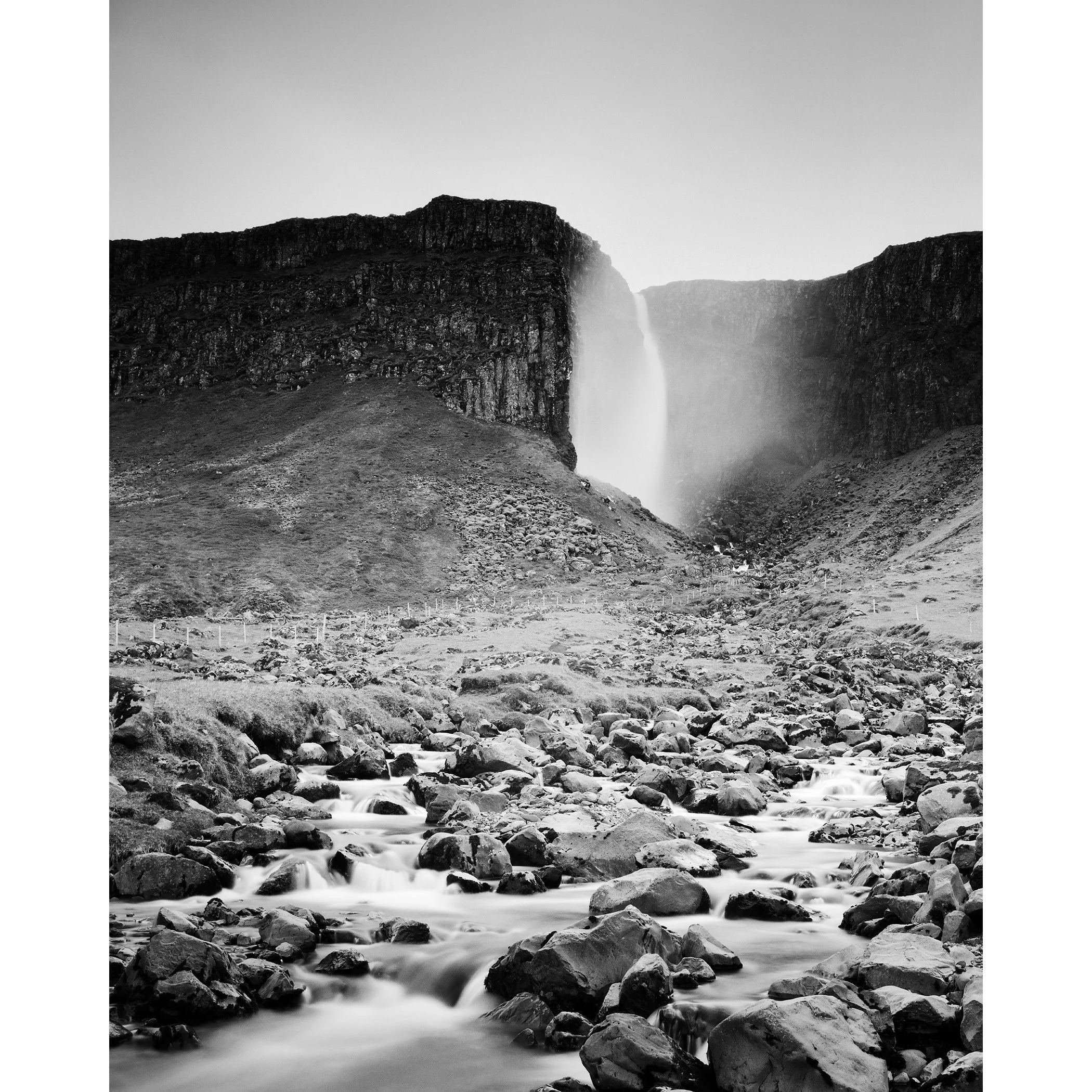 Gerald Berghammer - Black and white landscape photography. A waterfall cascading down a rocky cliff into a stream surrounded by rocks and rugged terrain.