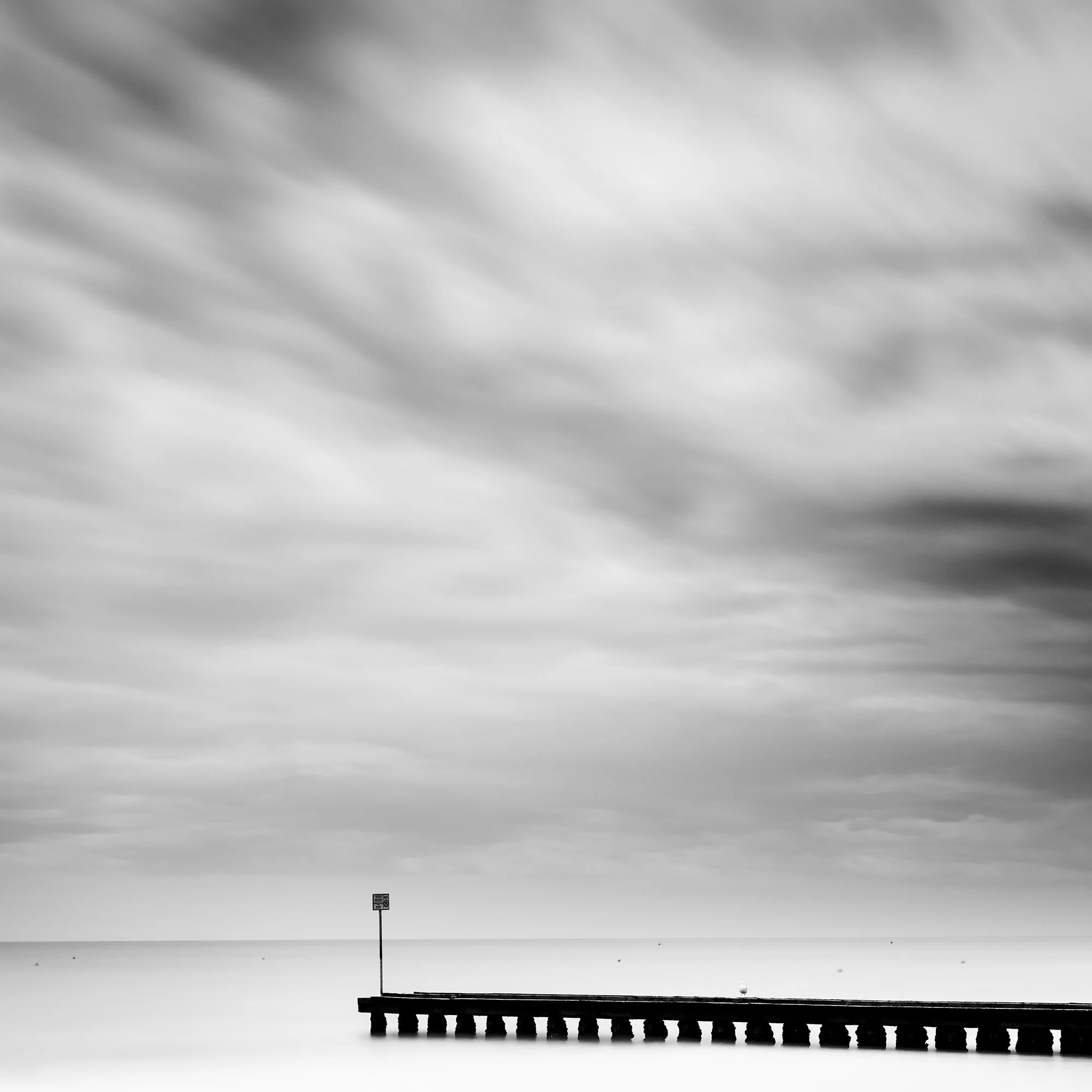 Wooden Pier in the Sea Study 1 – cropped detail of the wooden pier, calm sea and dramatic clouds in Italy by Gerald Berghammer.