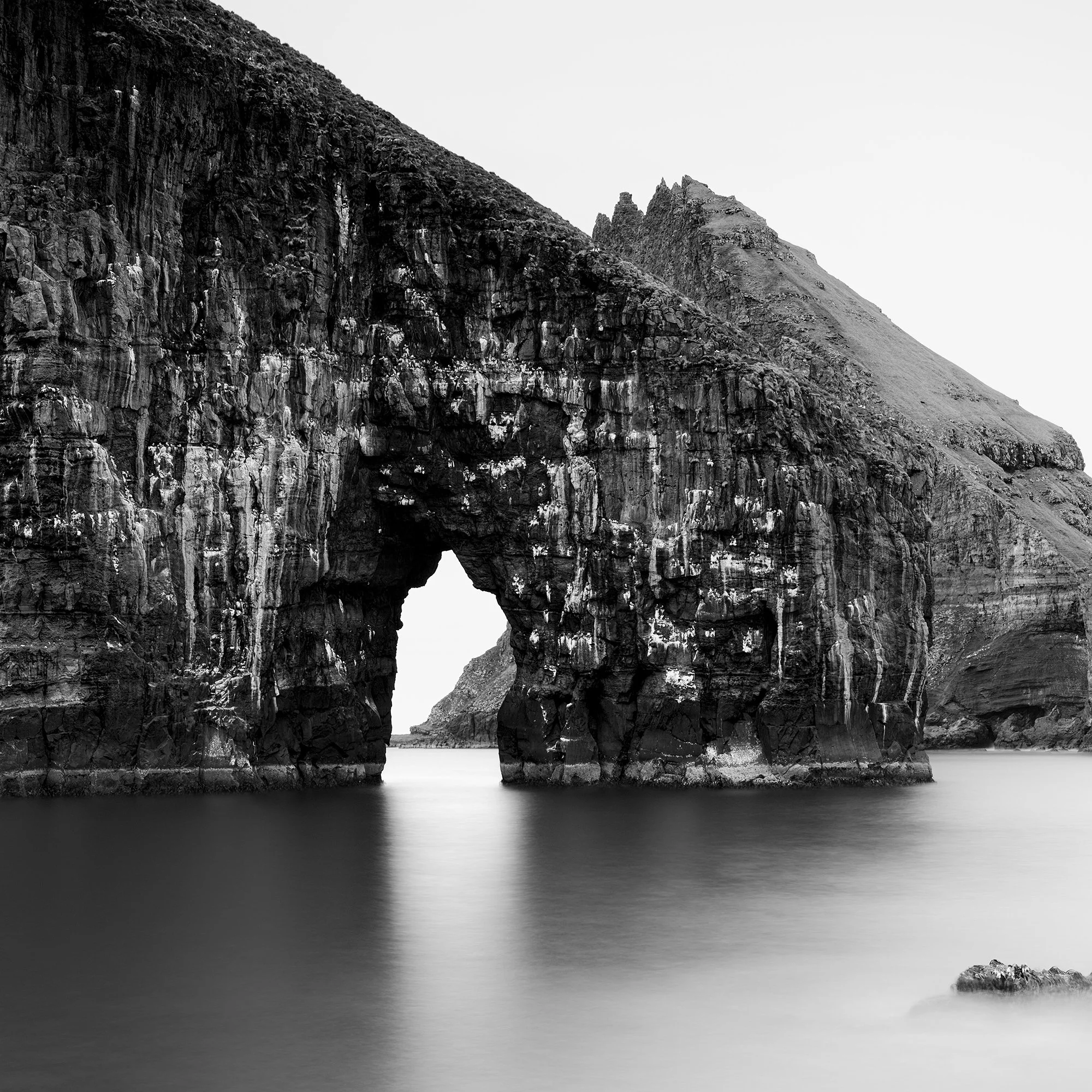Black and white coastal landscape with a striking sea stack arch and soft long-exposure water – zoomed-in view