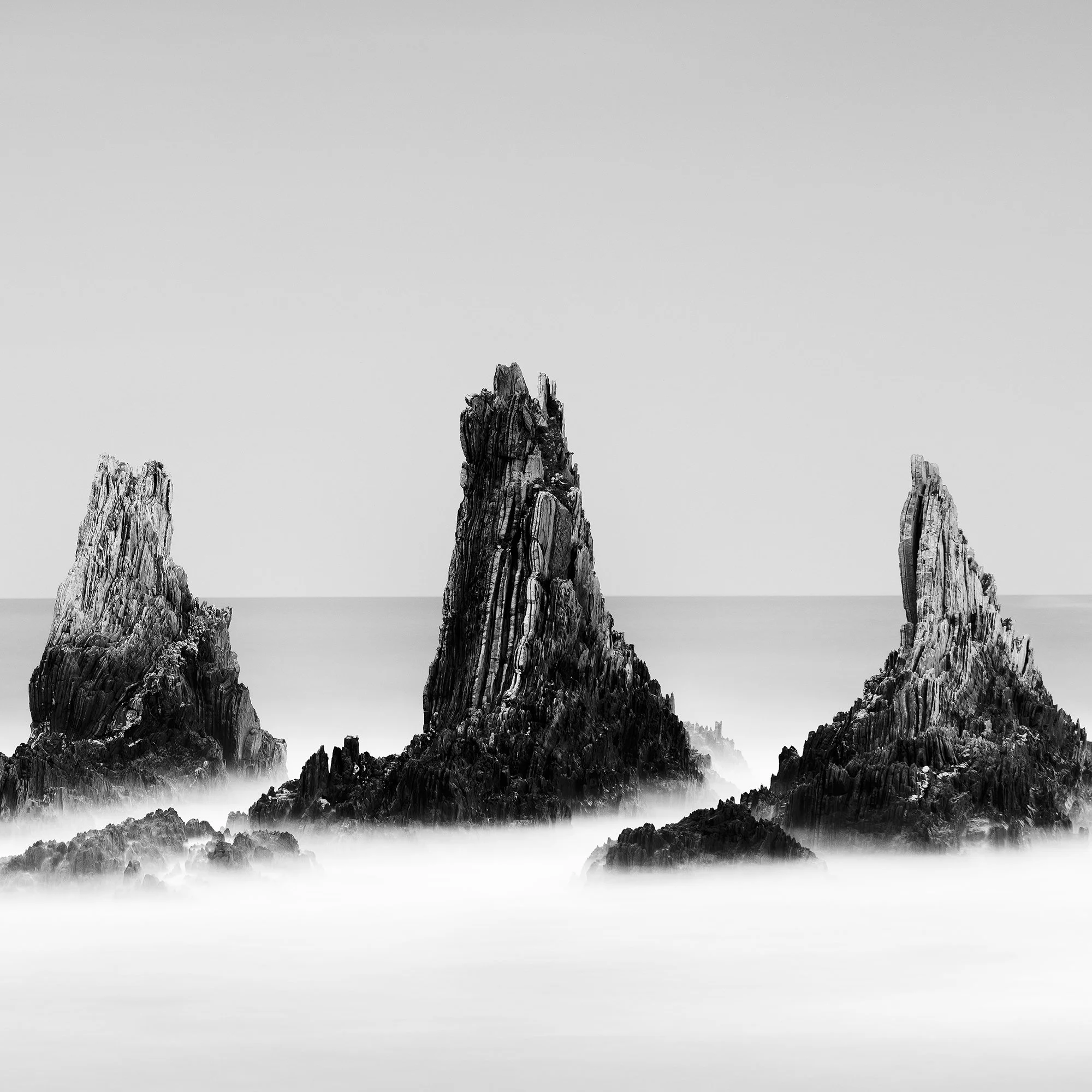 Rocky Peaks, Panorama Study 3 – detail of dark sea stacks rising from smooth long-exposure water in Spain by Gerald Berghammer.