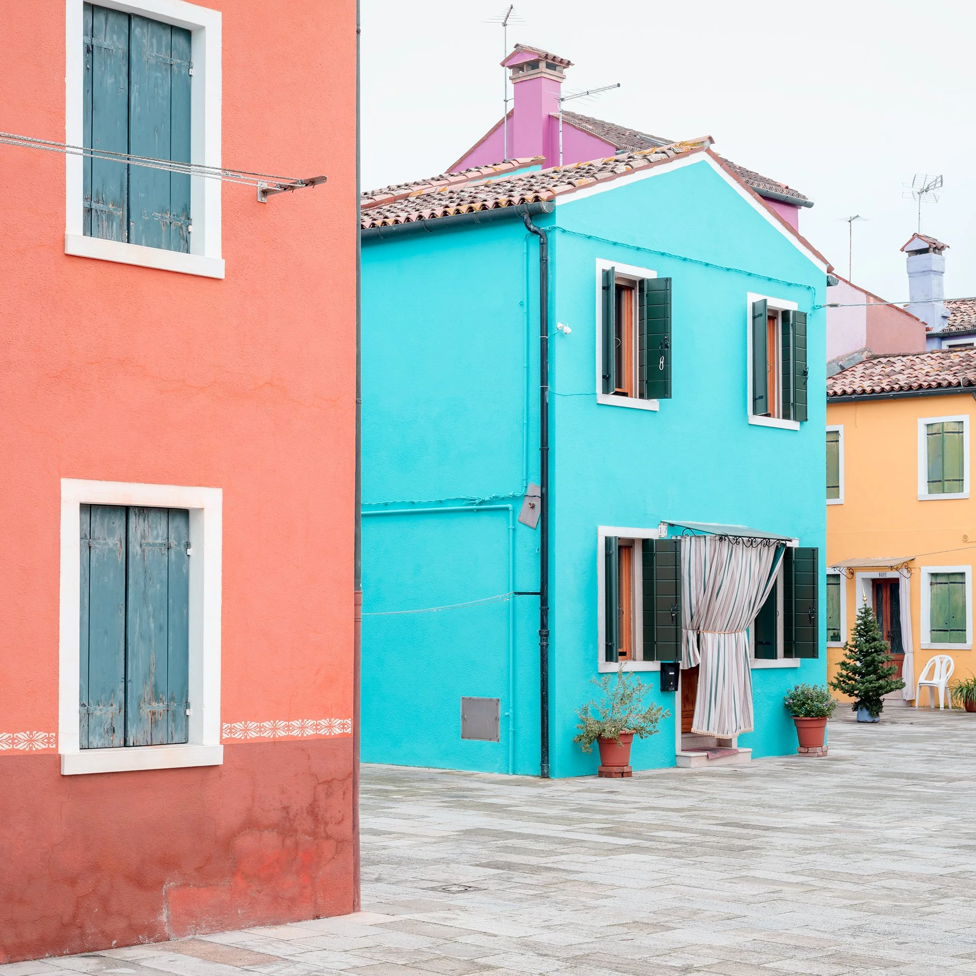 © 2025 Gerald Berghammer - Color cityscape photography. Colorful buildings with pastel pink, blue, yellow, and red walls, windows, and open shutters in a courtyard. Print detail 1