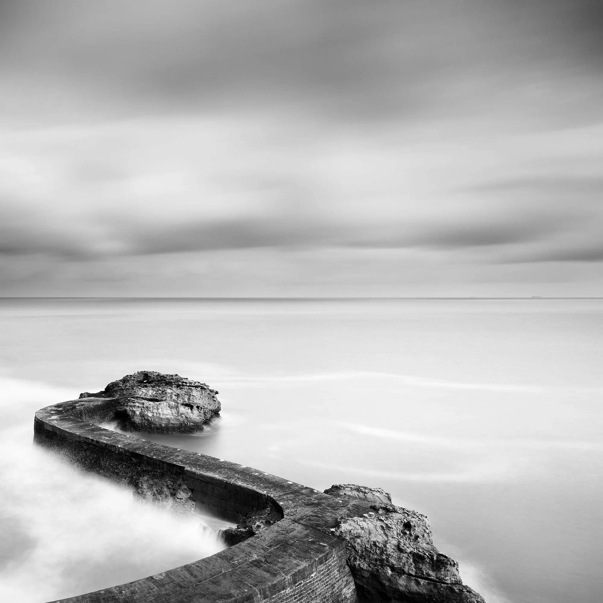 Breakwater Pier Study 1 by Gerald Berghammer, detail of weathered coastal rocks surrounded by smooth long-exposure seawater on the French Atlantic coast.