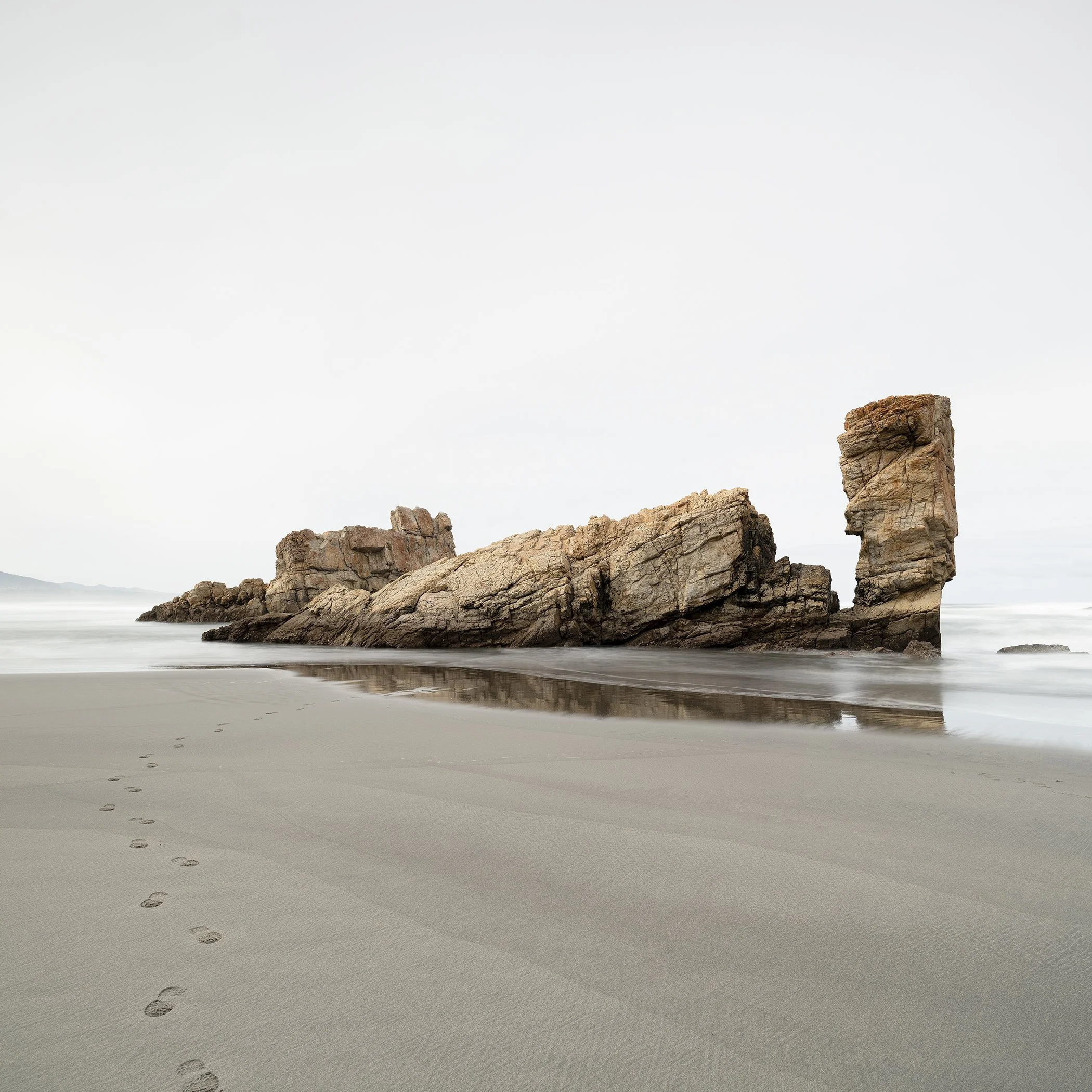 Minimalist colour seascape photograph of rock formations and reflections on an empty Bay of Biscay beach