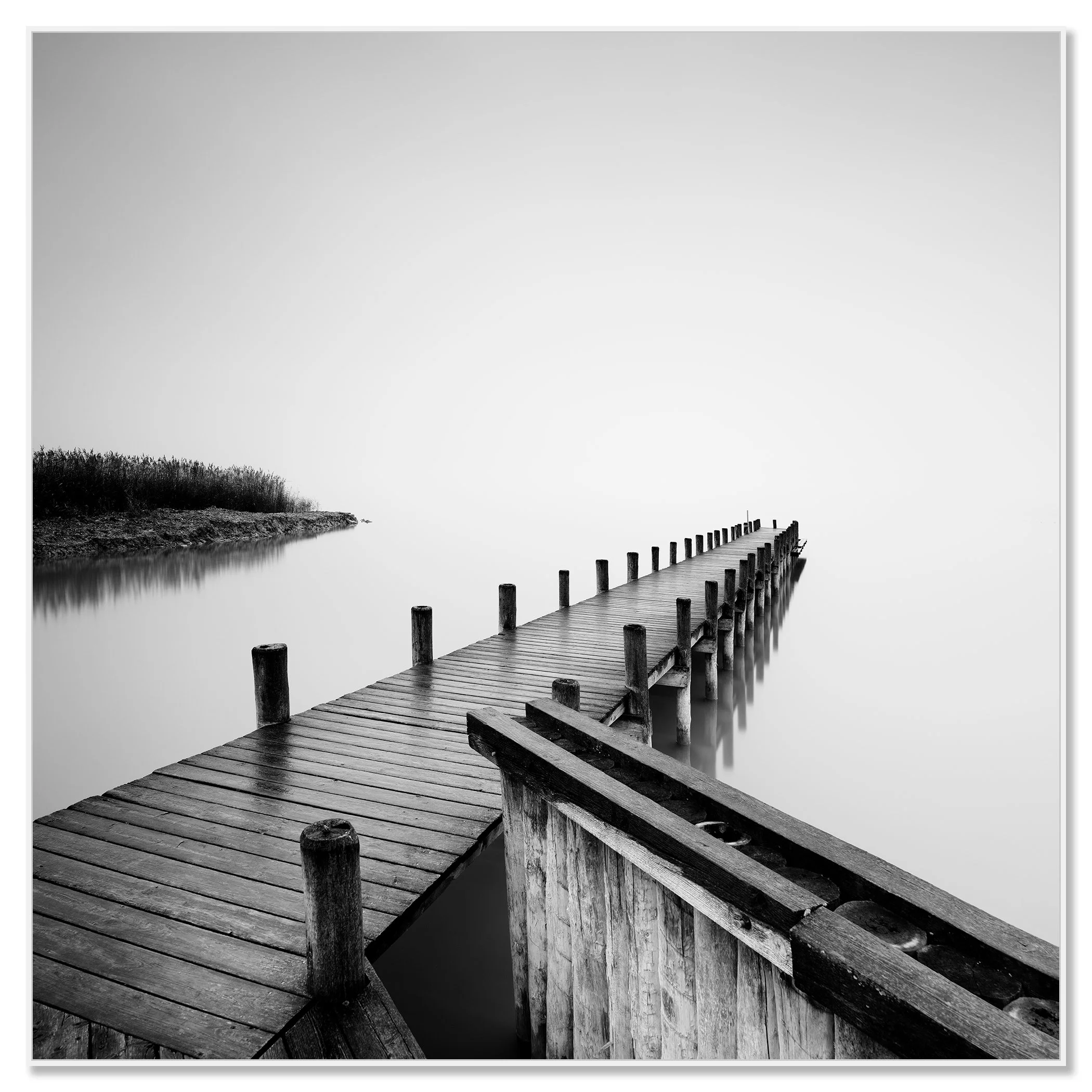 Gerald Berghammer - Black and white photography. Wooden pier extending out over calm water, with a foggy background and some reeds on the shoreline. Chromaluxe framed white