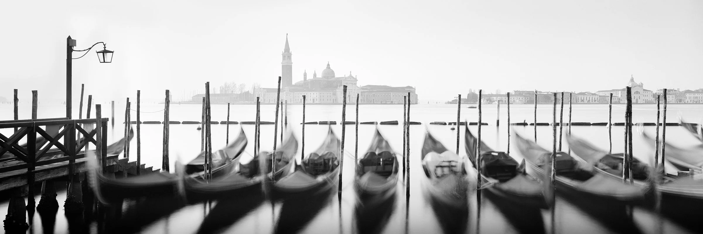 Black-and-white long-exposure photo of Venetian gondolas on the Venice waterfront, with silky smooth water and classic skyline.