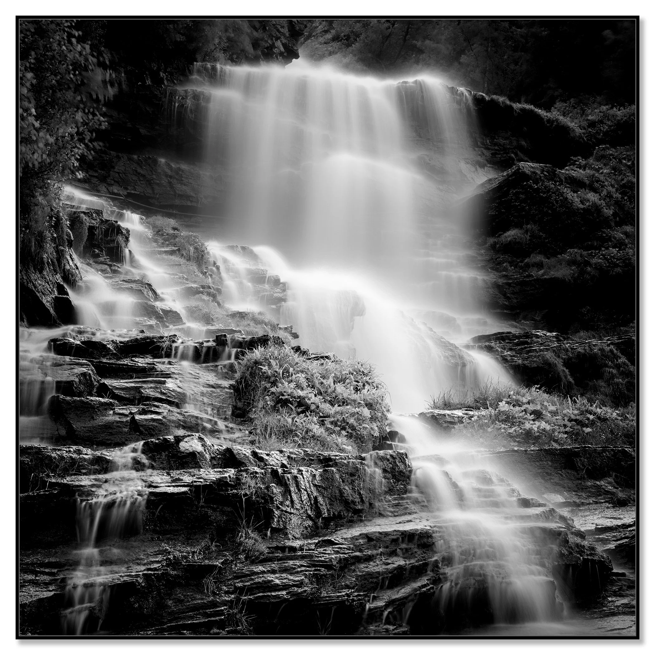 Multi-tiered waterfall cascading over rocks, framed by lush green vegetation – framed ArtBox black