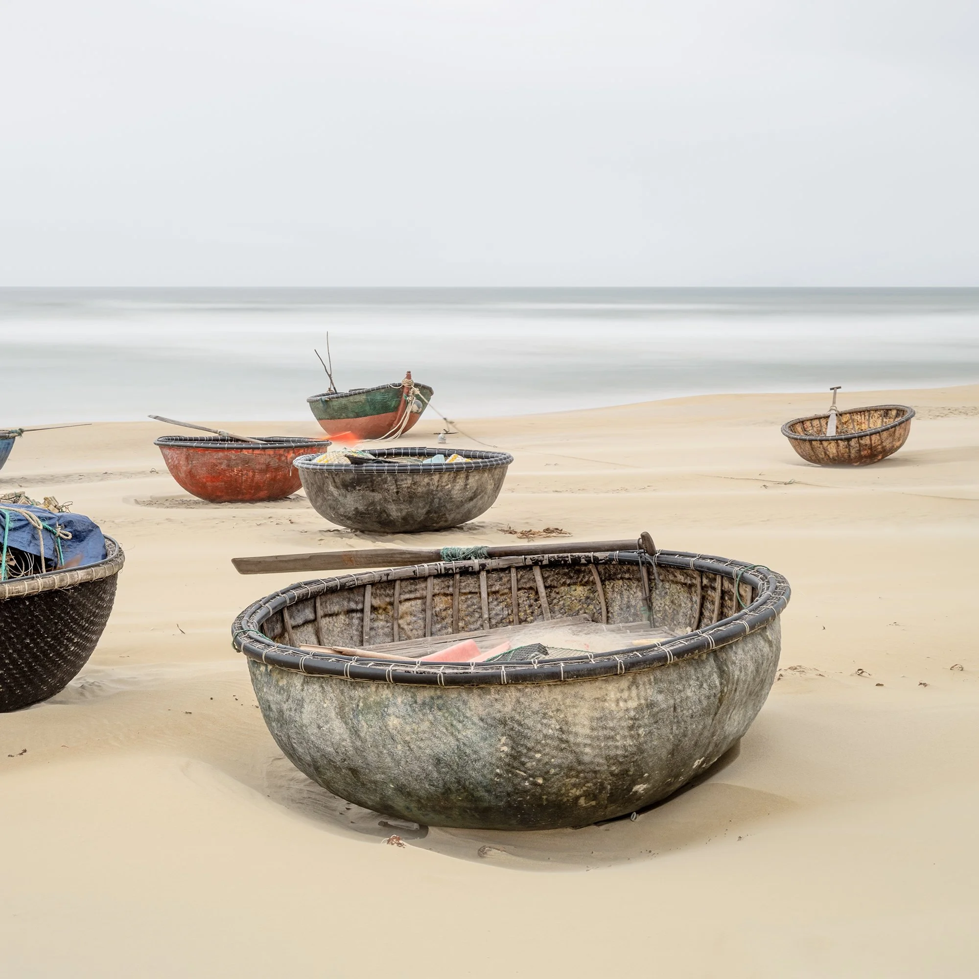 Gerald Berghammer - Color landscape photography. Several small boats resting on a sandy beach with calm ocean water under an overcast sky. Print detail 2