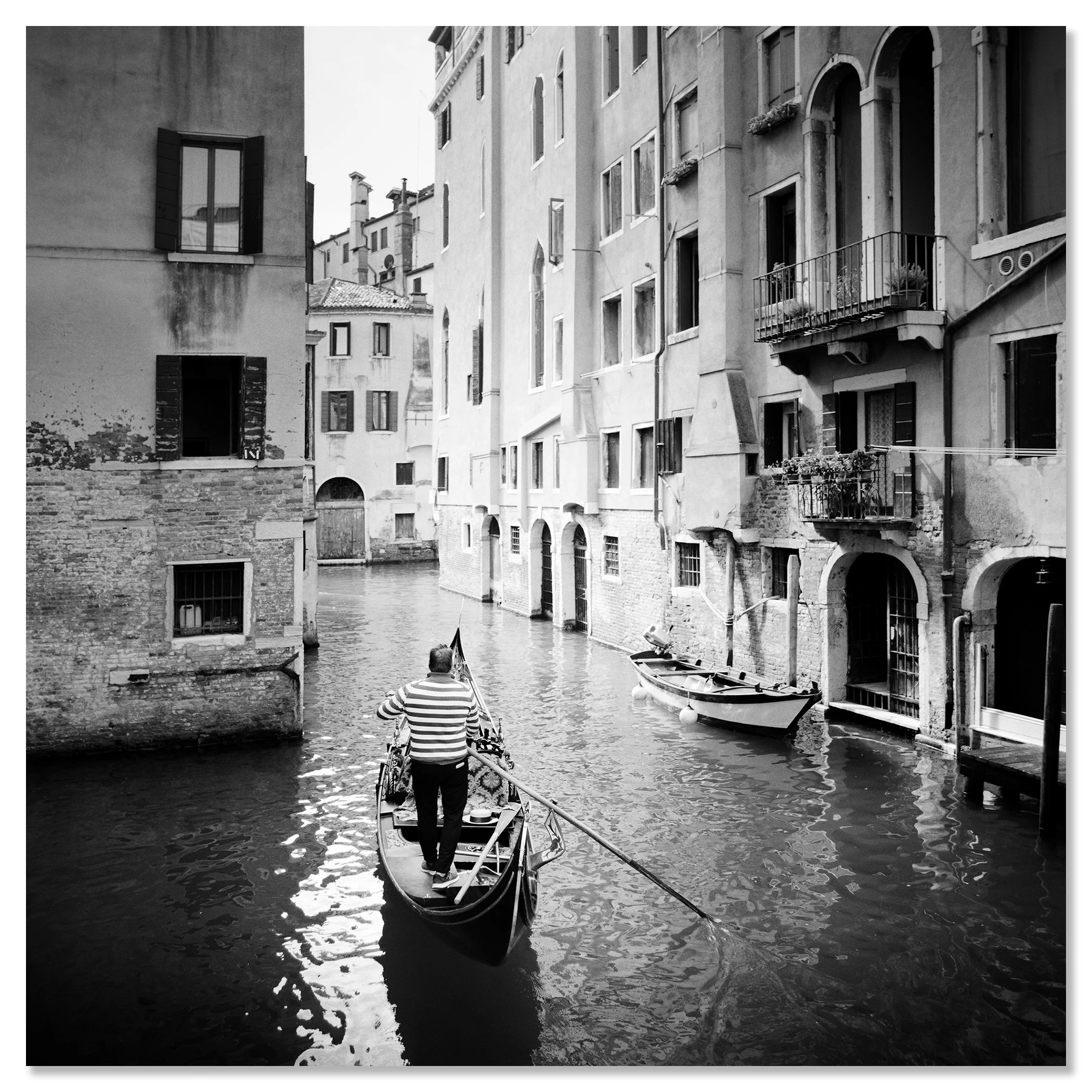 Gondolier rowing a gondola through a narrow canal in Venice, Italy, between tall historic buildings – dibond frameless