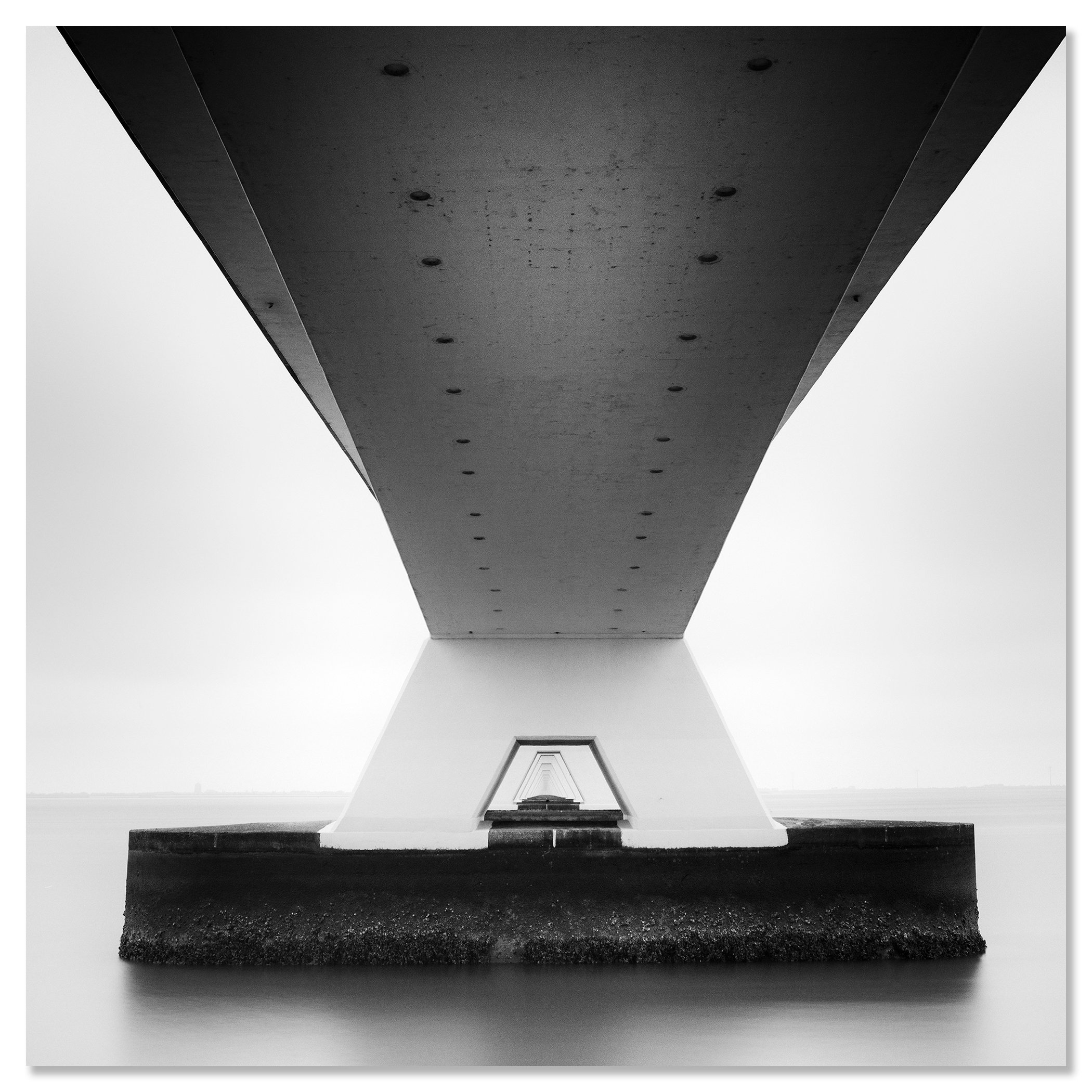 Gerald Berghammer - Black and white cityscape photo. Underneath view of a bridge with large support pillars, showing the underside and the water below. Chromaluxe frameless