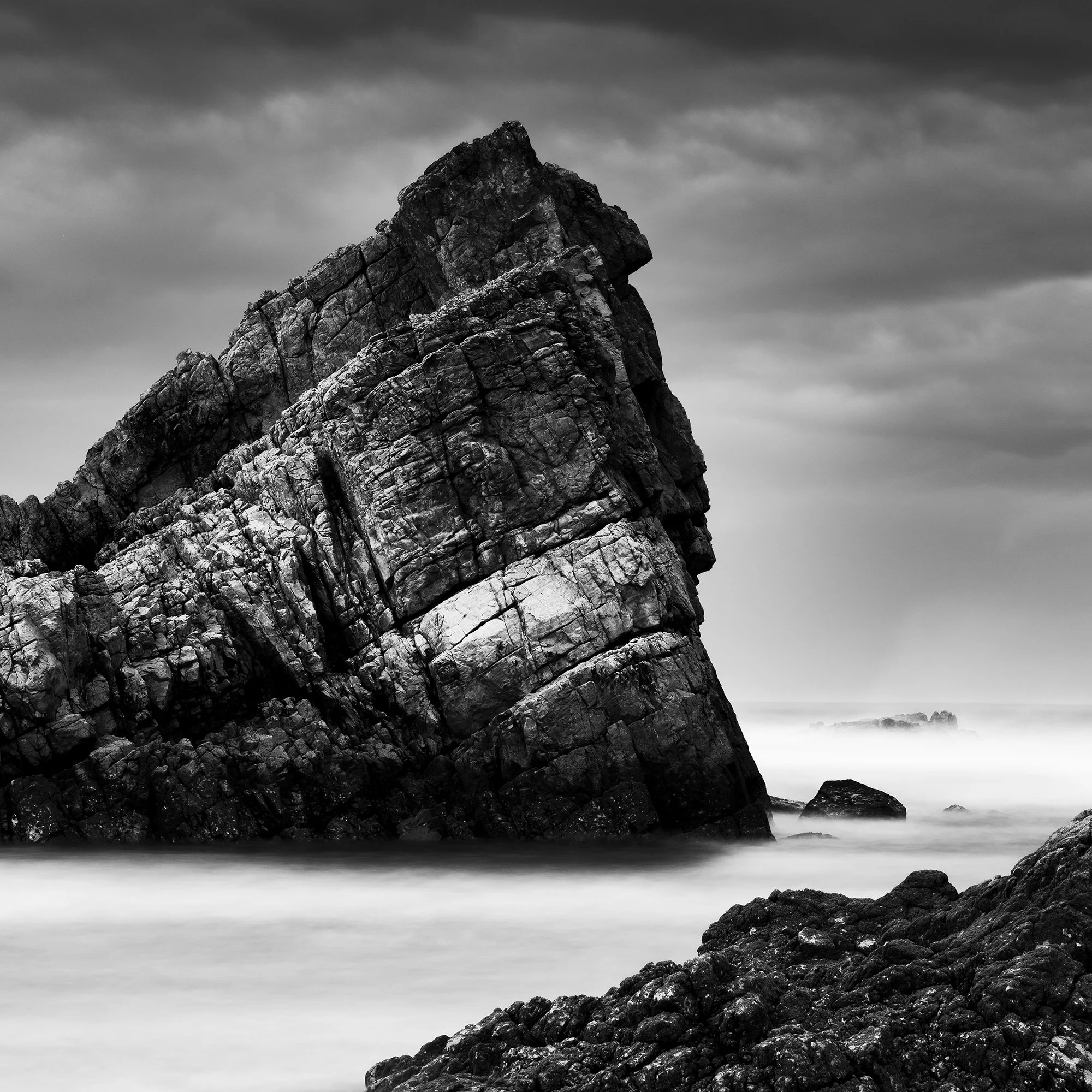 © 2023 Gerald Berghammer. Black-and-white photograph of jagged sea rocks emerging from calm water under a cloudy sky. Print detail 3