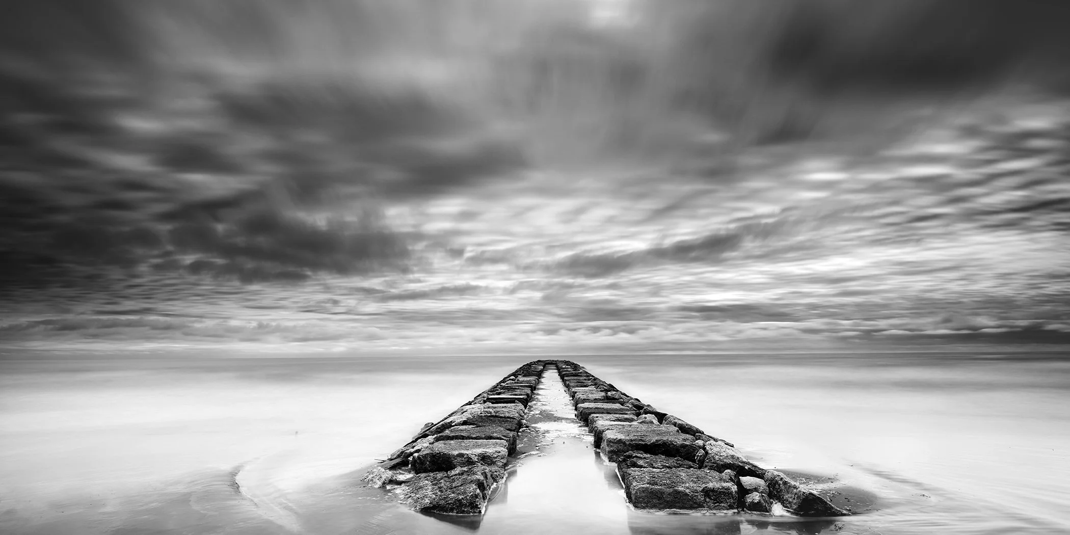 Rock Pier, Panorama Study 1 by Gerald Berghammer, minimalist black-and-white long-exposure panorama of a stone pier beneath dramatic clouds in Italy.