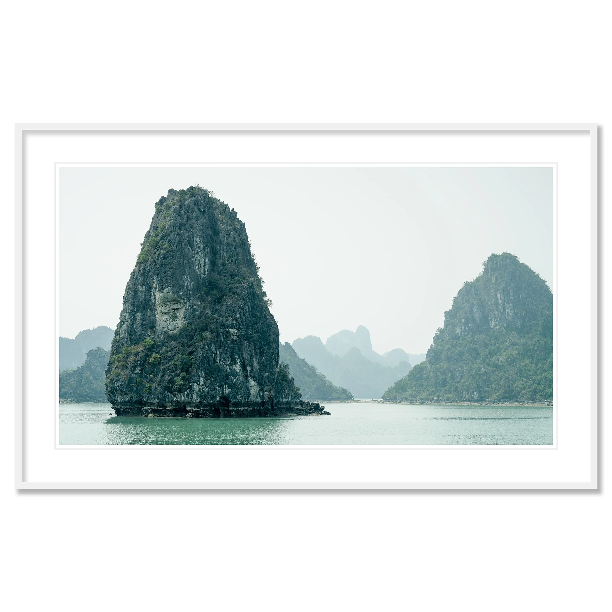 Gerald Berghammer - Color Seascape Photography. Limestone karst formations rise from the water in a tranquil bay, with hazy mountains, Southeast Asia. Classic framed white