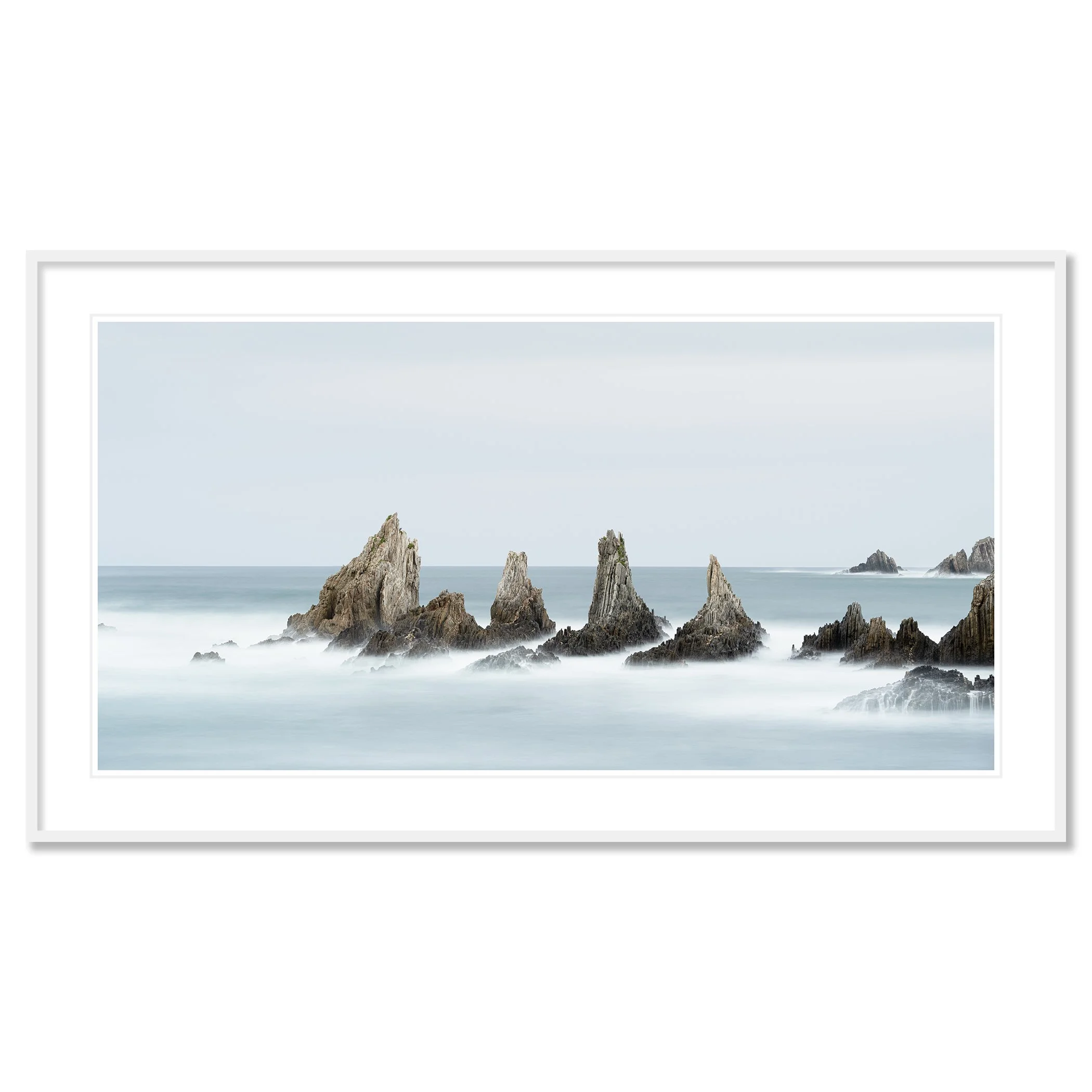 Gerald Bergammer - Color minimalist seascape photography. Long exposure photo of jagged rocks in the ocean with misty water and a cloudy sky. Classic framed white