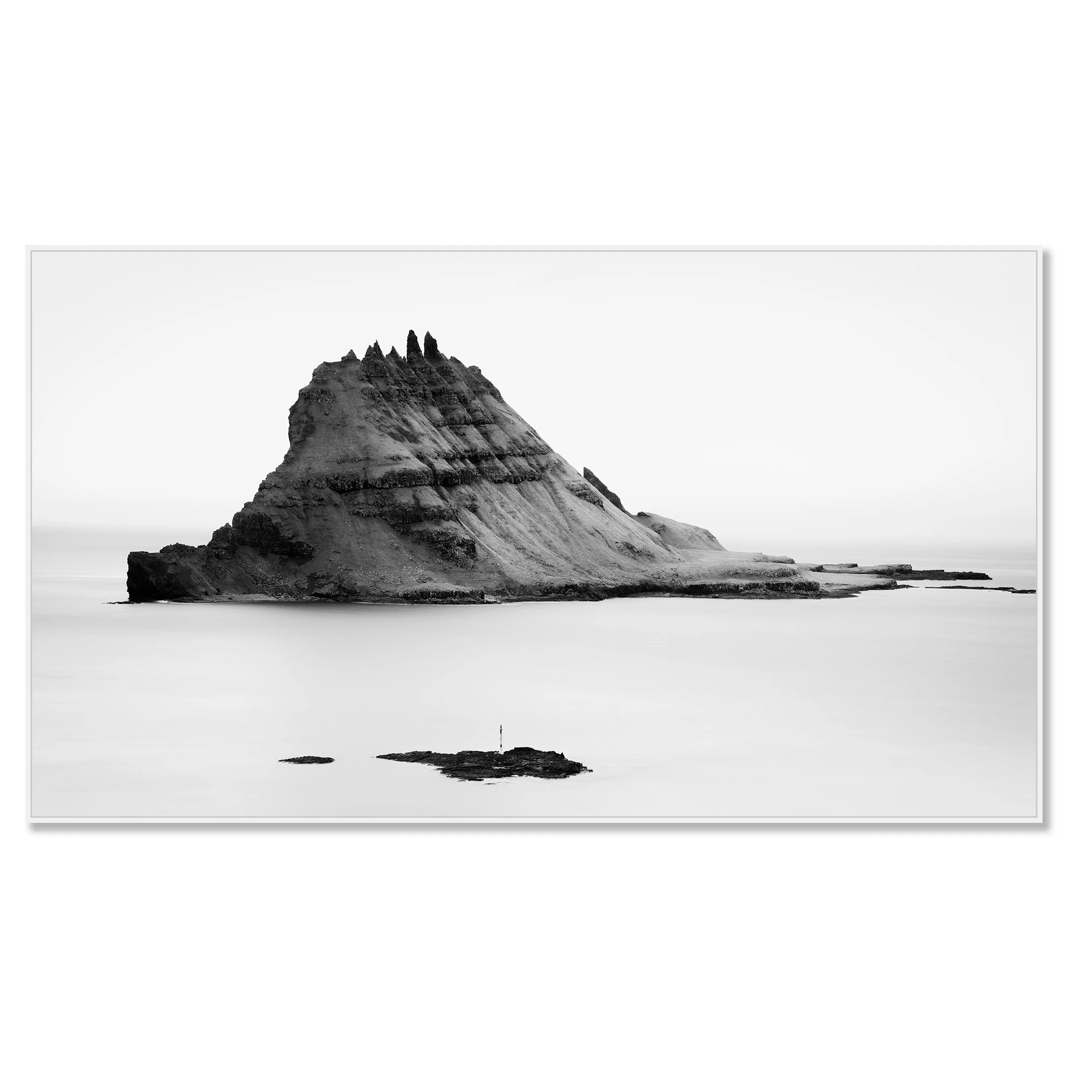 Black-and-white panoramic photo of a layered sea stack in the ocean, with smaller rocks in the foreground and waves – framed ArtBox white