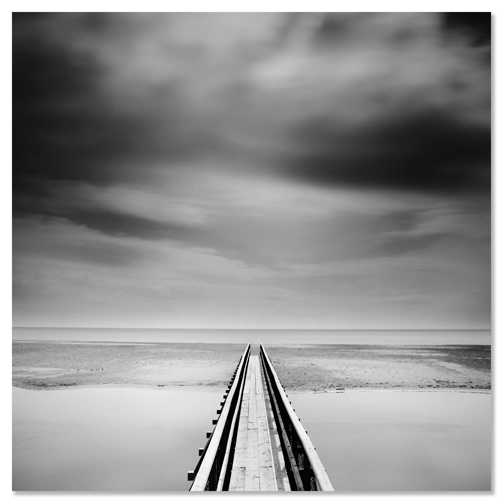 Minimalist monochrome seascape with a narrow pier centred in perspective stretching to the horizon beneath an overcast sky – dibond frameless