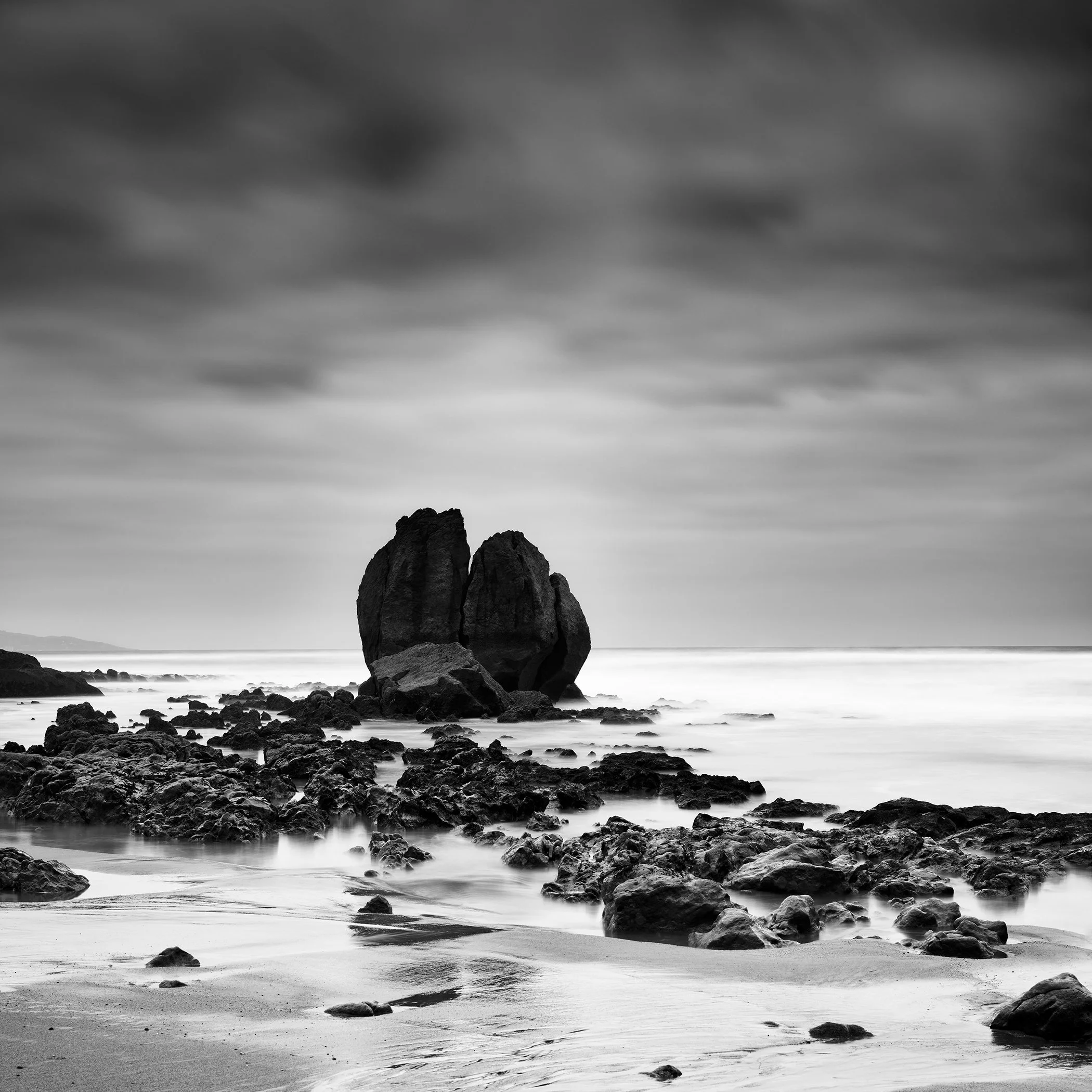 Monochrome coastal landscape featuring a dramatic rock formation surrounded by sea and shoreline