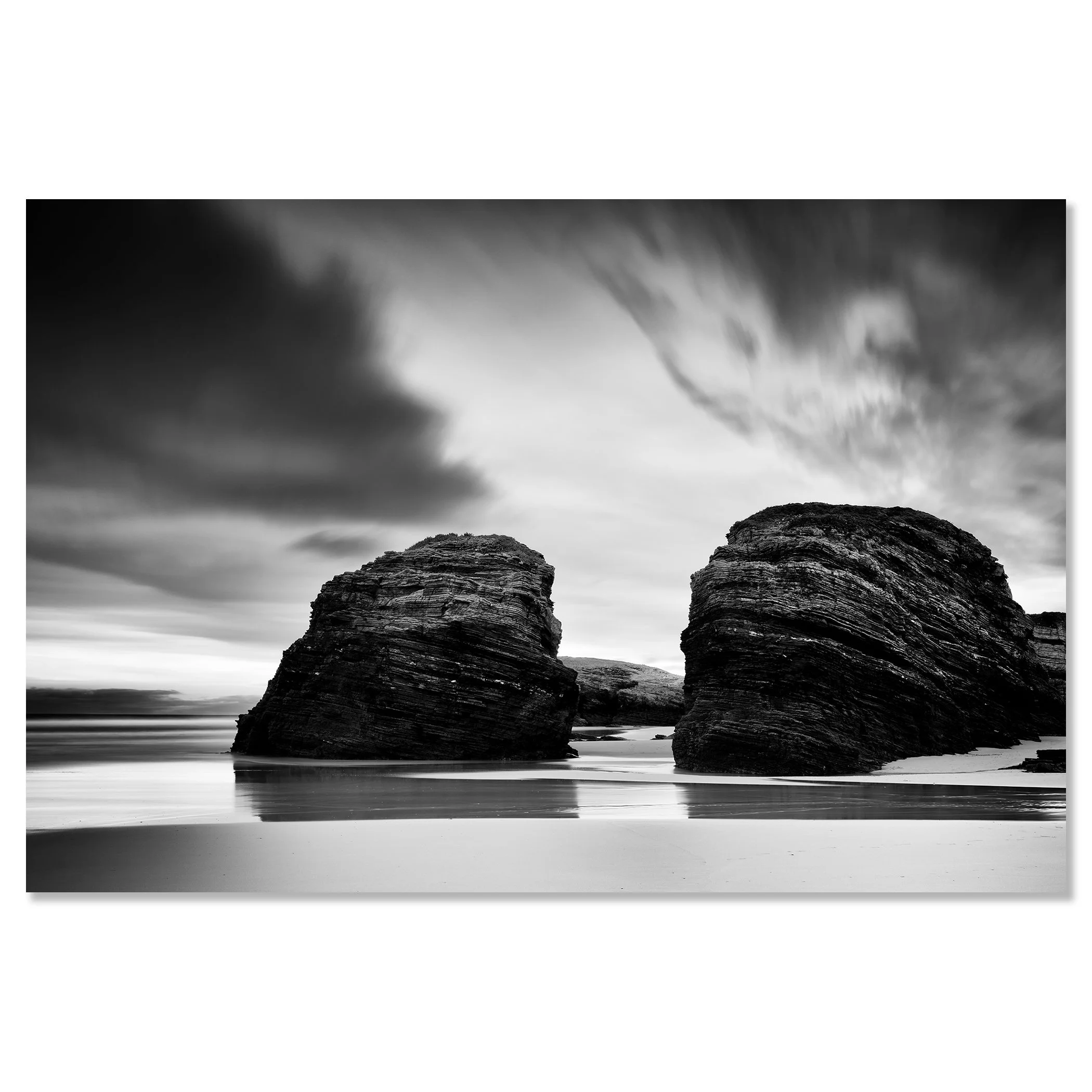 Black and white seascape with two rounded rocks on a beach beneath a cloudy sky – dibond frameless