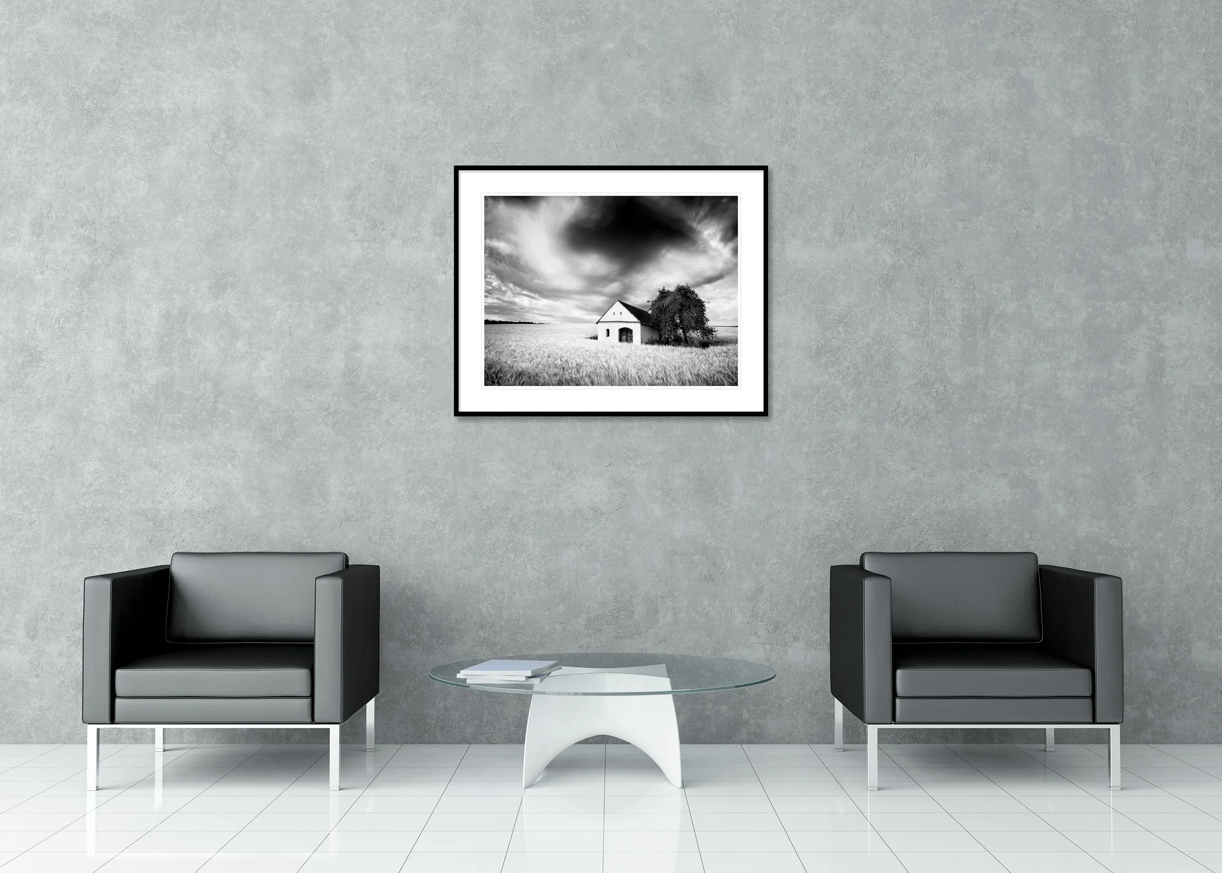 Black-and-white photograph of the Wine Press House in a wheat field beneath dramatic storm clouds, archival pigment print in a classic frame with passe-partout.