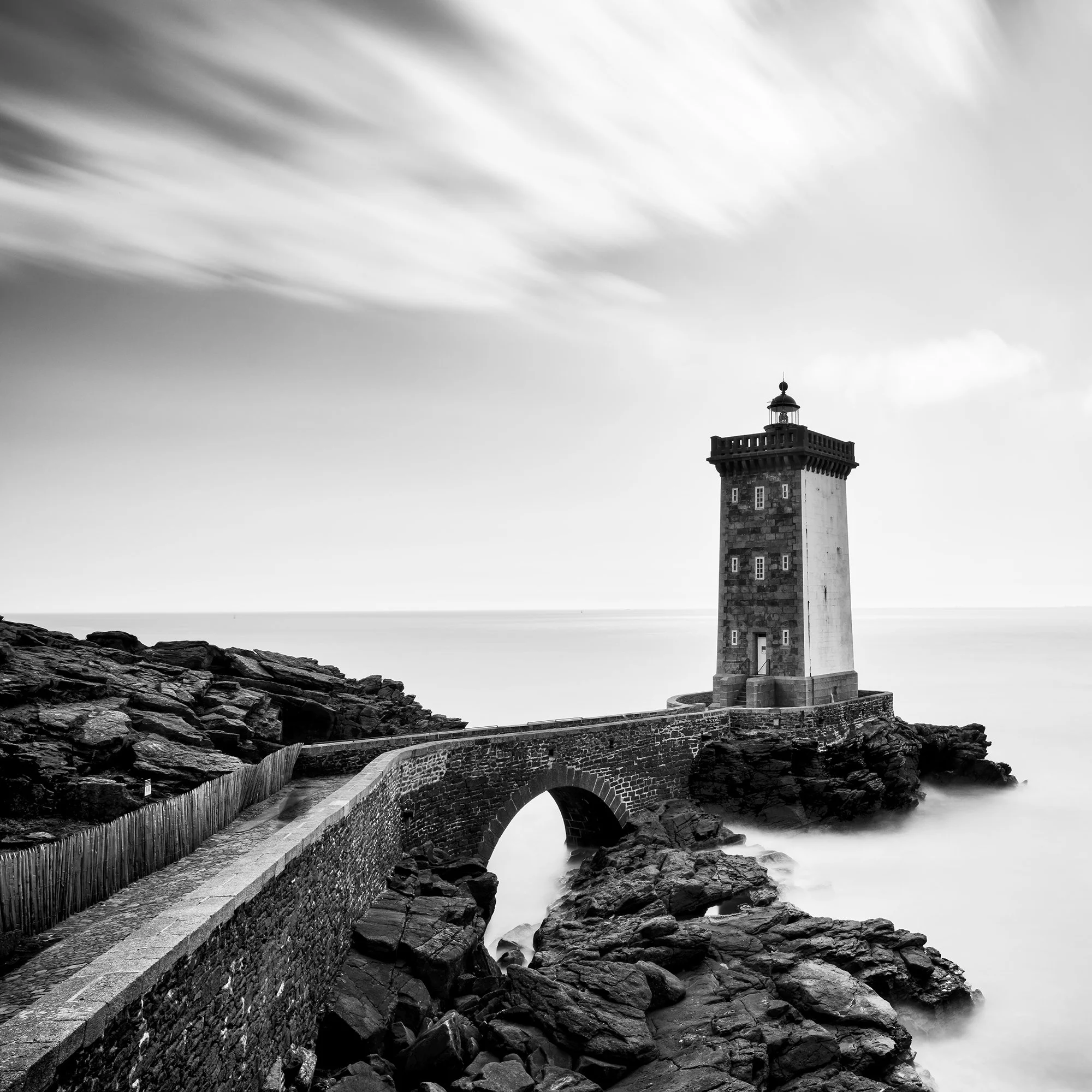 Lighthouse of Kermorvan by Gerald Berghammer, detailed black-and-white view of the stone bridge, lighthouse and rocky Atlantic coastline.