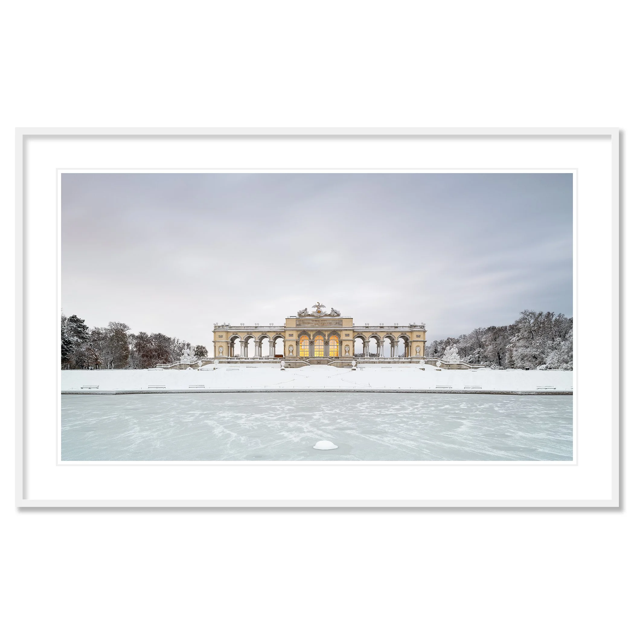 Gerald Berghammer - Color Photography. A historic building on a snow-covered landscape, surrounded by leafless trees, with a frozen body of water. Classic framed white