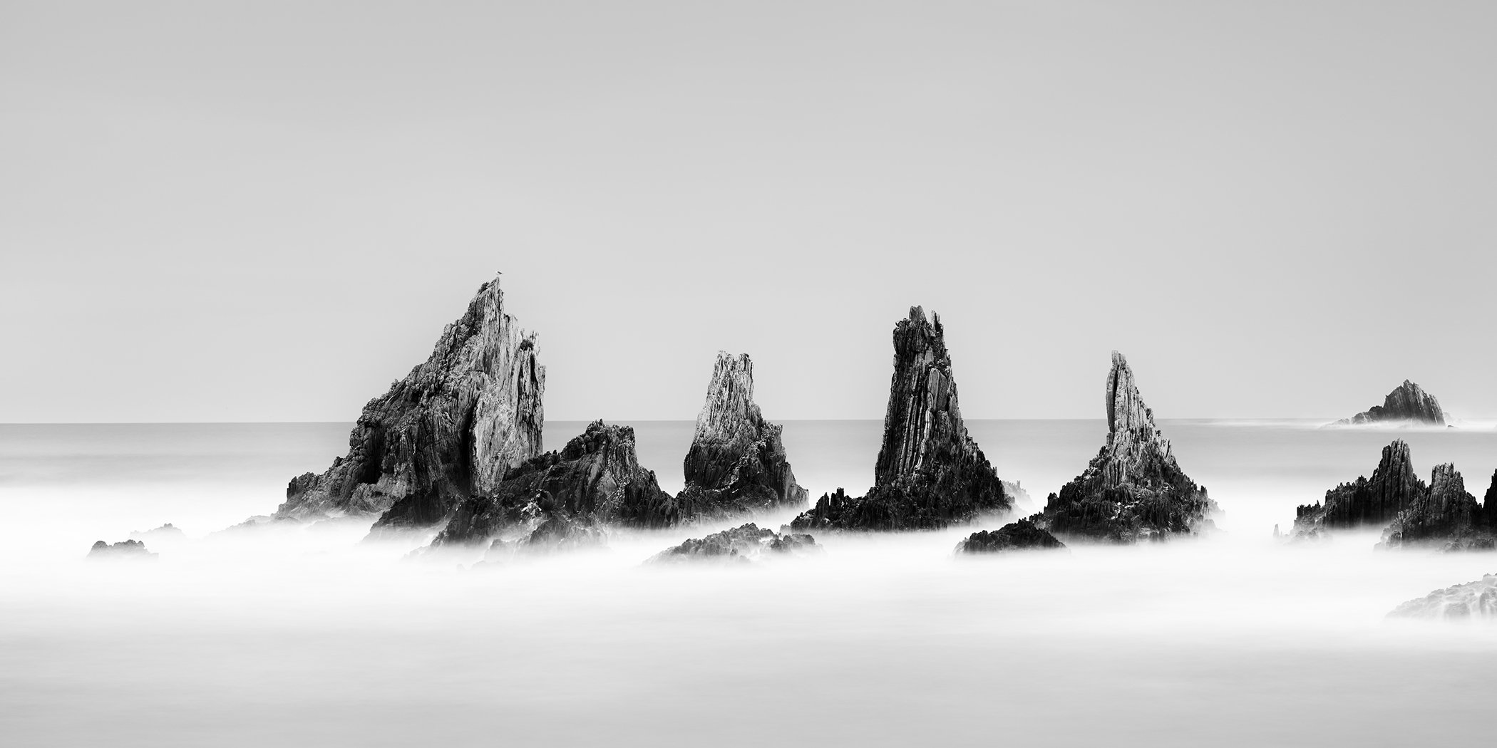 Rocky Peaks Panorama, Study 2 – panoramic black-and-white seascape of jagged rock formations and mist-like ocean in Spain by Gerald Berghammer.