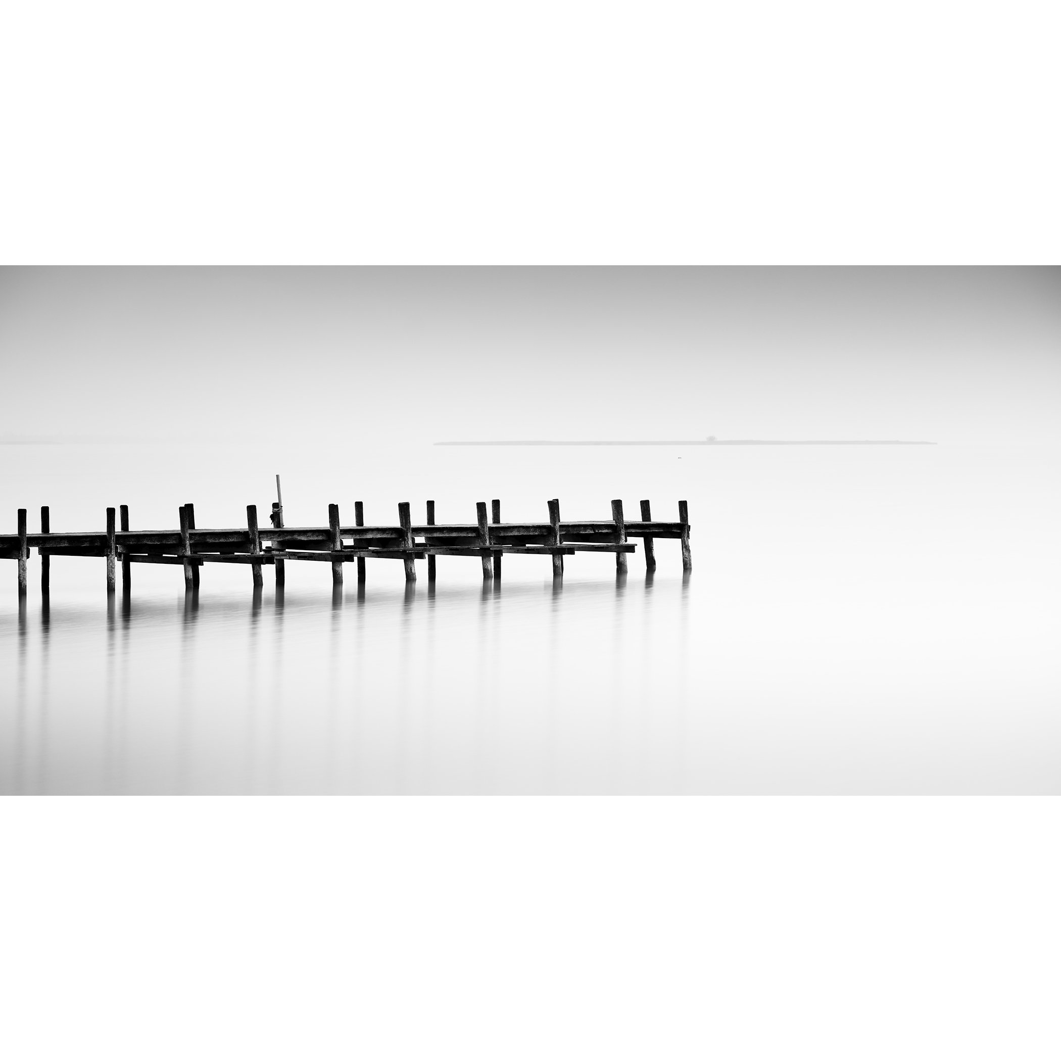 © 2023 Gerald Berghammer - Black and white long exposure waterscape photo. Wooden pier extending into calm water, with a minimalistic and serene background.