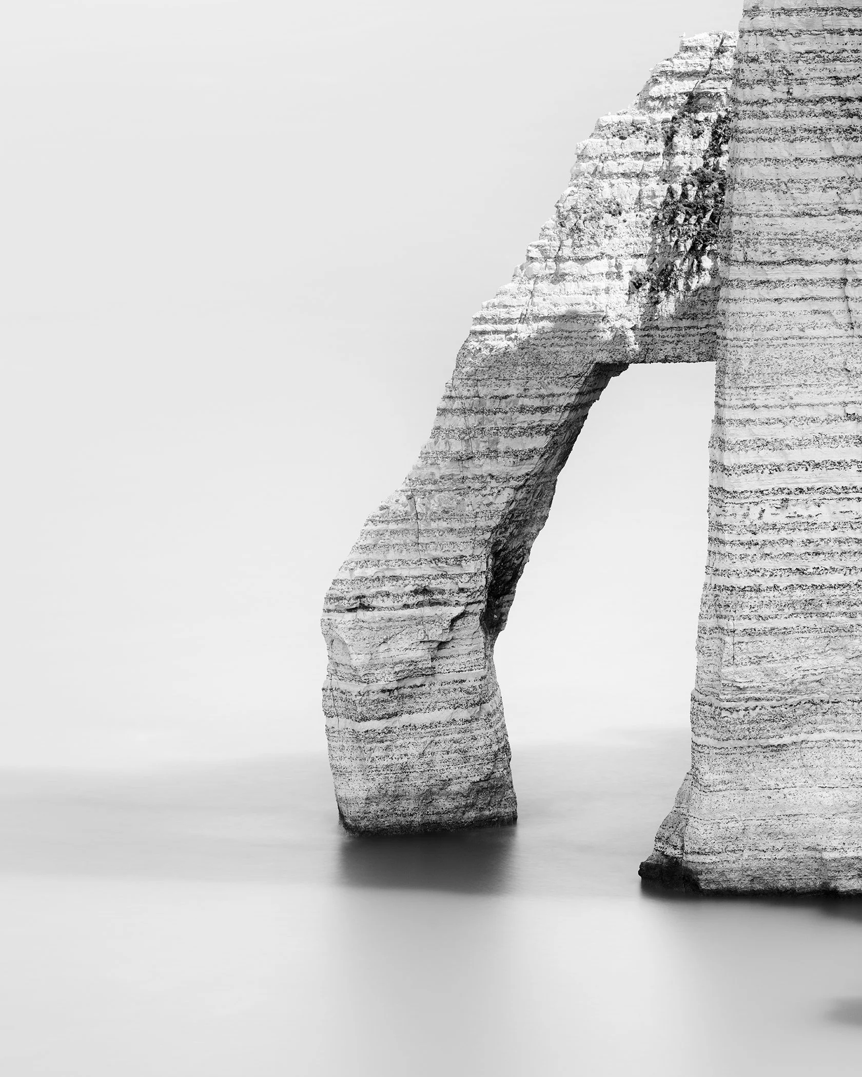 Abstract black and white image of a rough stone sculpture in an arch shape with subtle shadows and a minimalist composition.