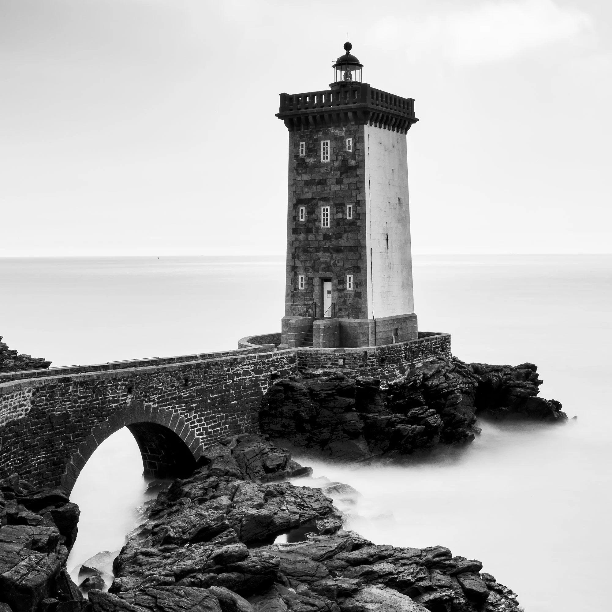 Lighthouse of Kermorvan by Gerald Berghammer, close-up photograph of the stone lighthouse, arched bridge and coastal rocks.