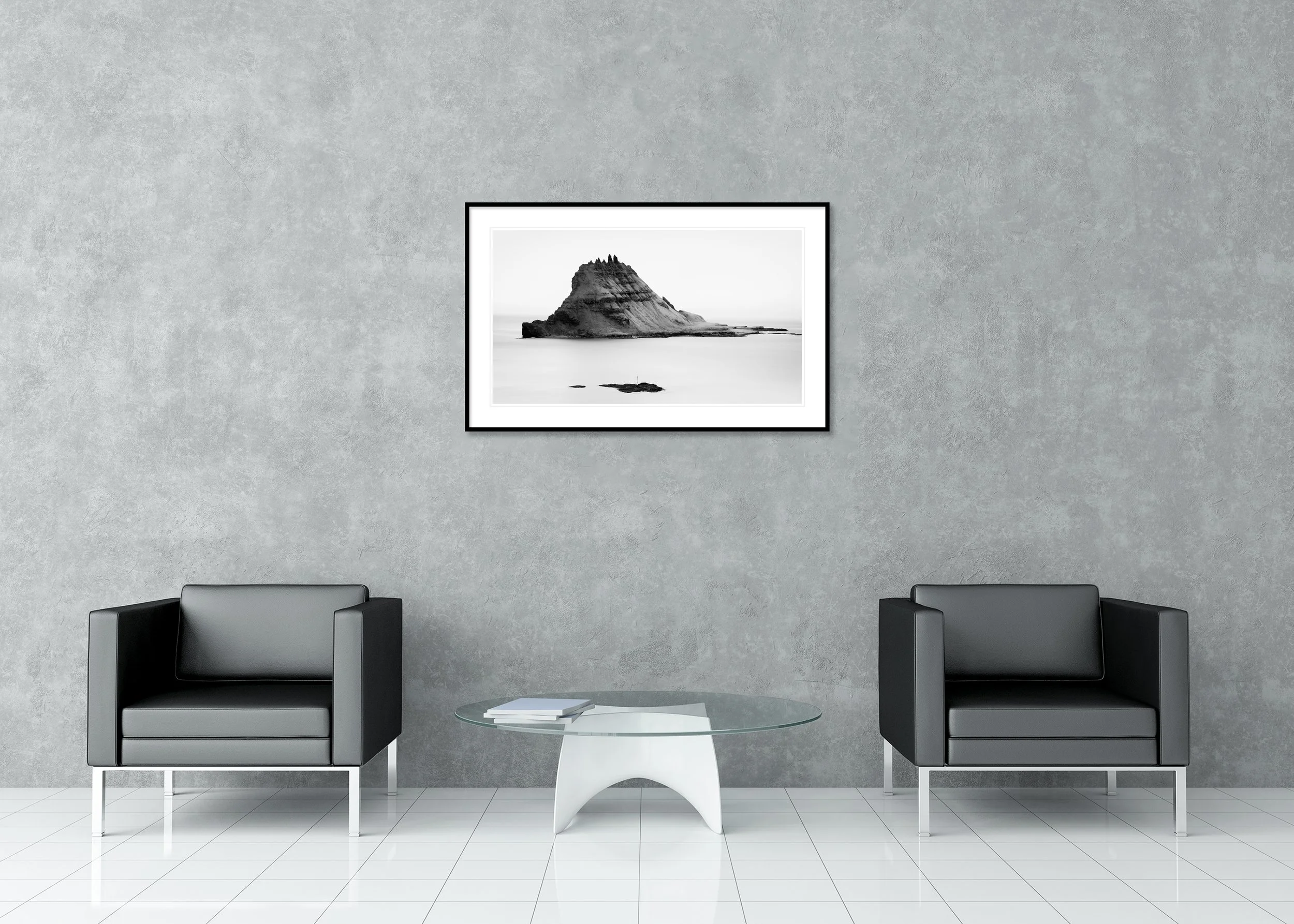 Black and white long-exposure photograph of a rugged rocky island rising from a calm sea beneath a minimalist sky, as an archival pigment print in a classic frame with mount.