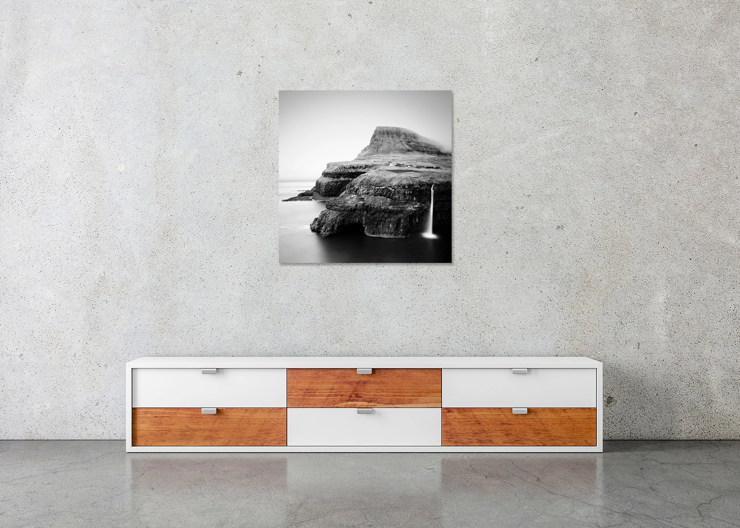 Black-and-white photo print of a Faroe Islands coastal cliff with waterfall flowing into the ocean near a remote village, mounted to Dibond, frameless.
