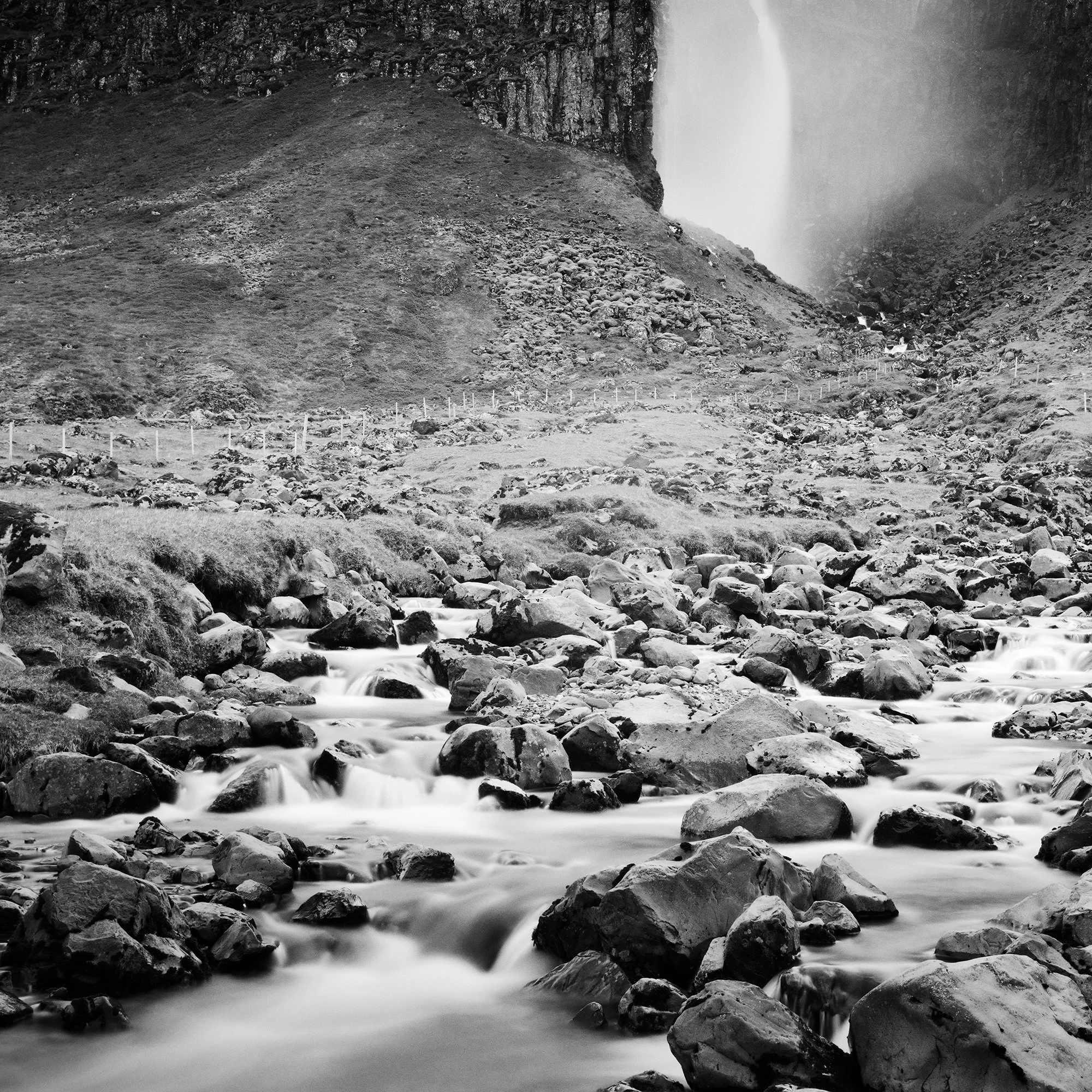 Gerald Berghammer - Black and white landscape photography. A waterfall cascading down a rocky cliff into a stream surrounded by rocks and rugged terrain. Print detail 1