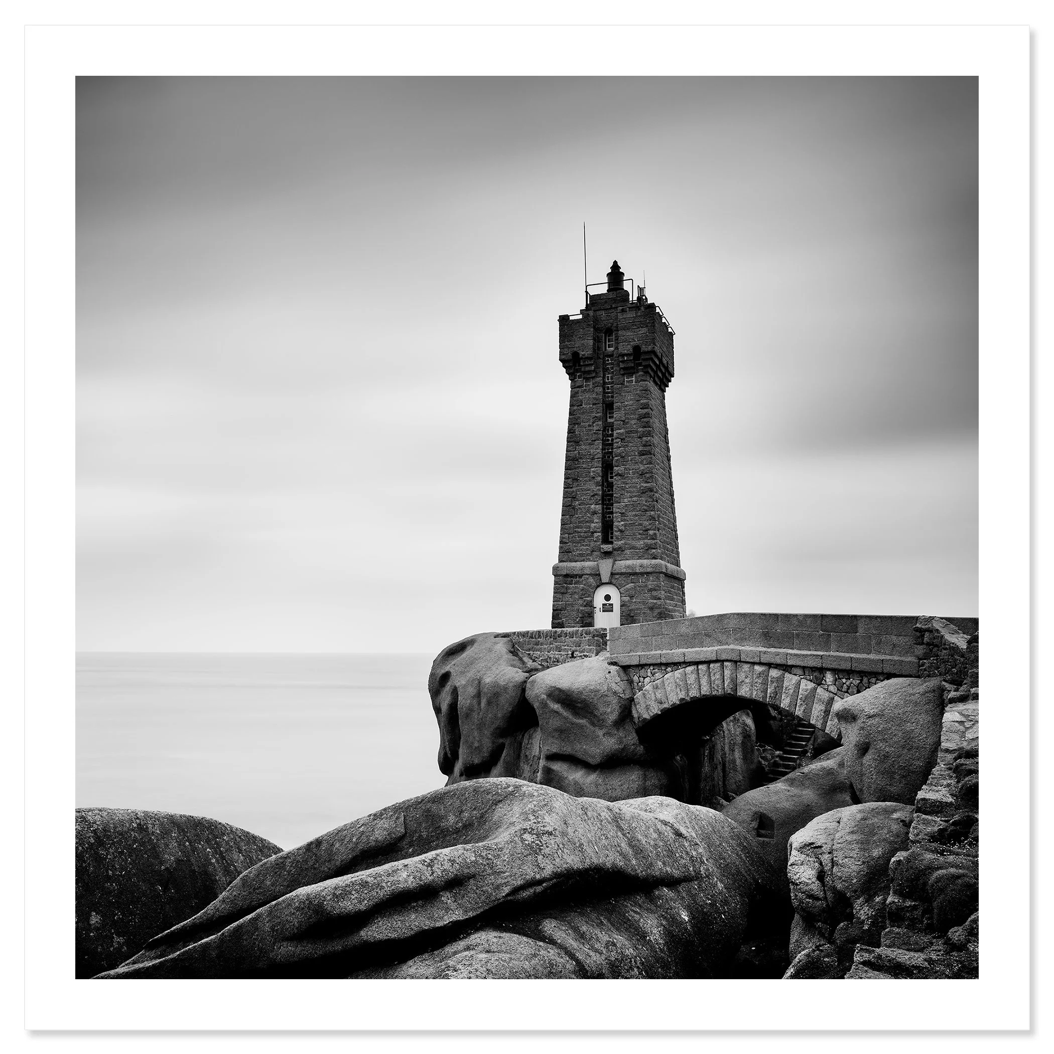 Gerald Berghammer - Black and white landscape photograph of a tall lighthouse on a rocky coast, with a small bridge and large rocks in foreground. Fine art print only
