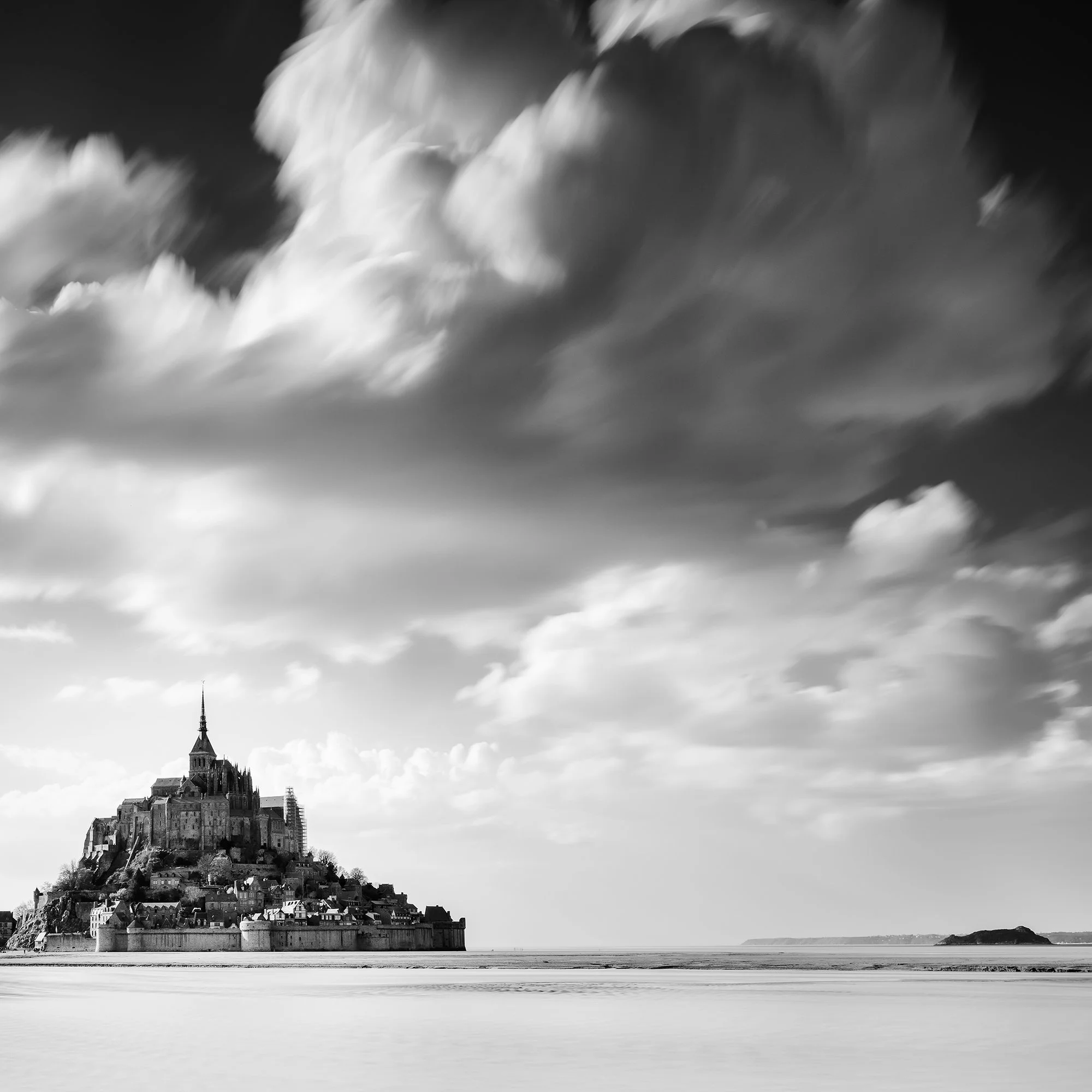 Detail of Mont-Saint-Michel beneath sweeping clouds in this black-and-white photograph by Gerald Berghammer.