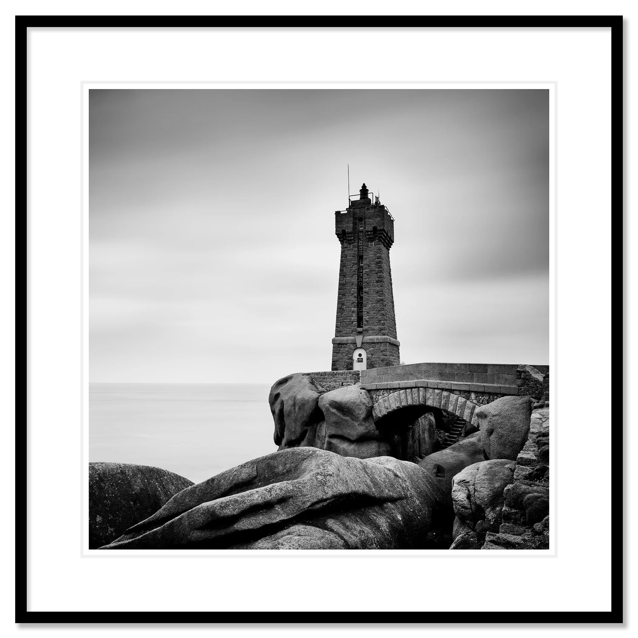 Gerald Berghammer - Black and white landscape photograph of a tall lighthouse on a rocky coast, with a small bridge and large rocks in foreground. Classic framed black
