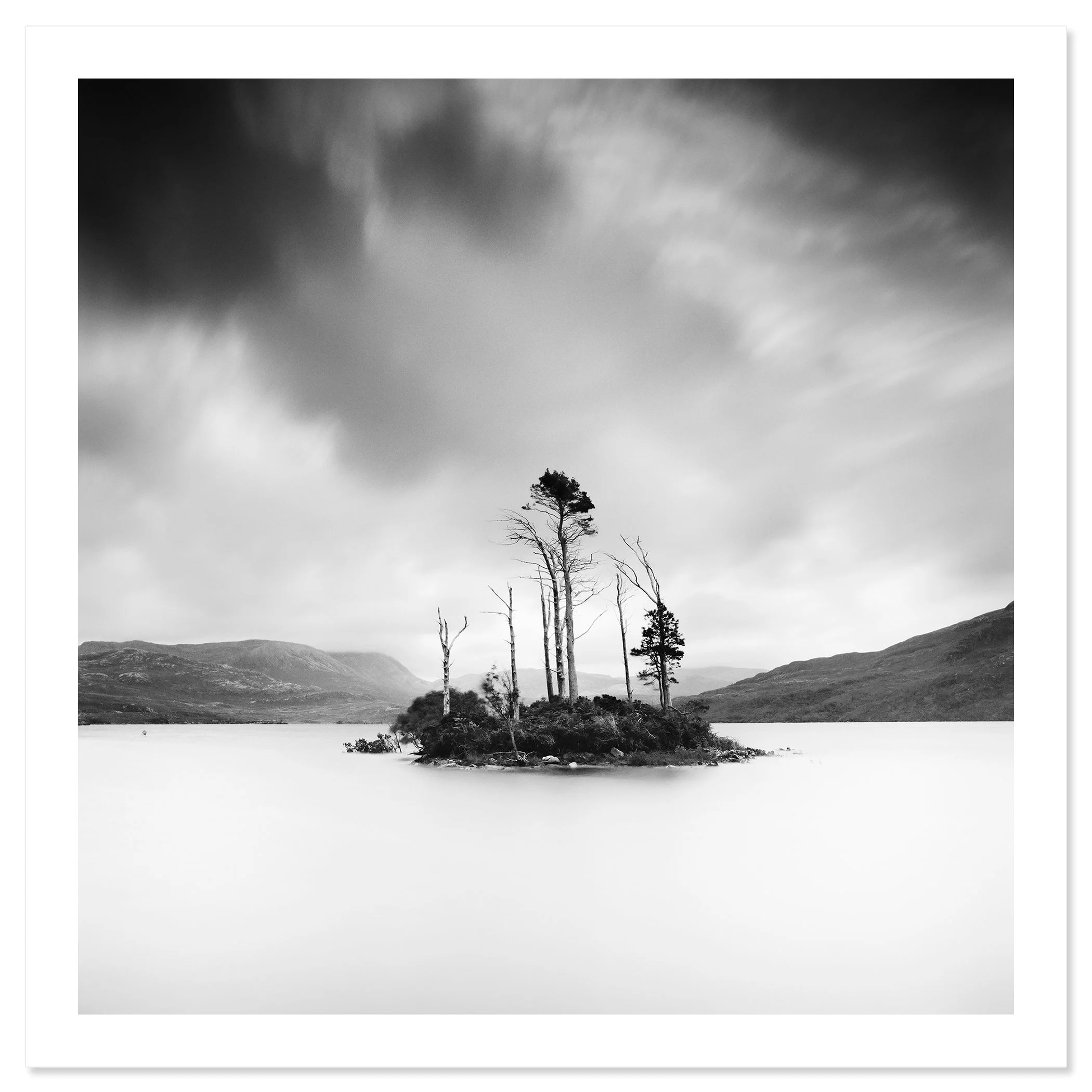 © 2012 Gerald Berghammer - Black and white waterscape photography. Small island with tall, thin trees surrounded by water and distant mountains under a cloudy sky. Fine art print only