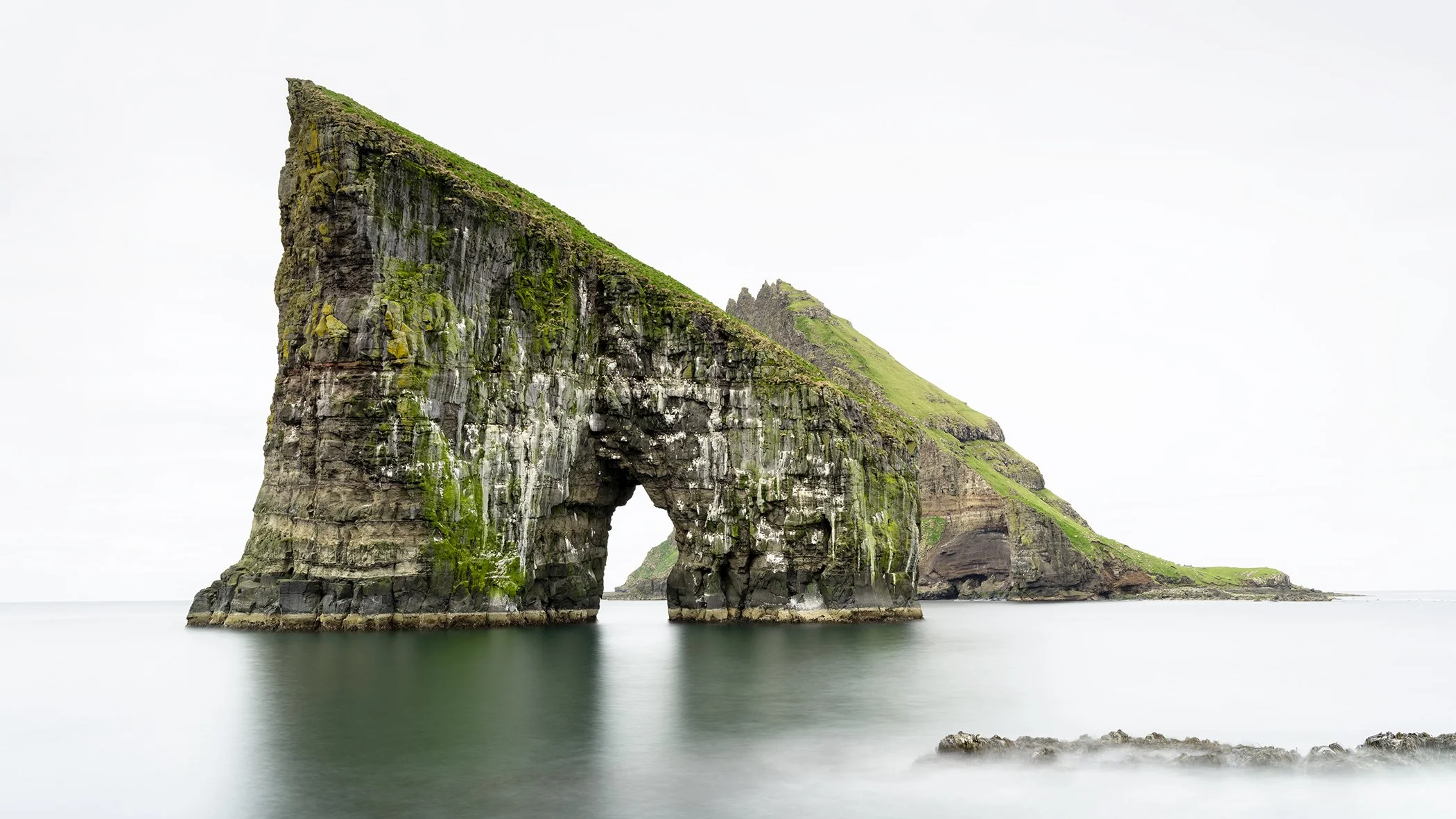 Drangarnir Sea Arch rising from calm water in a minimalist Faroe Islands seascape by Gerald Berghammer