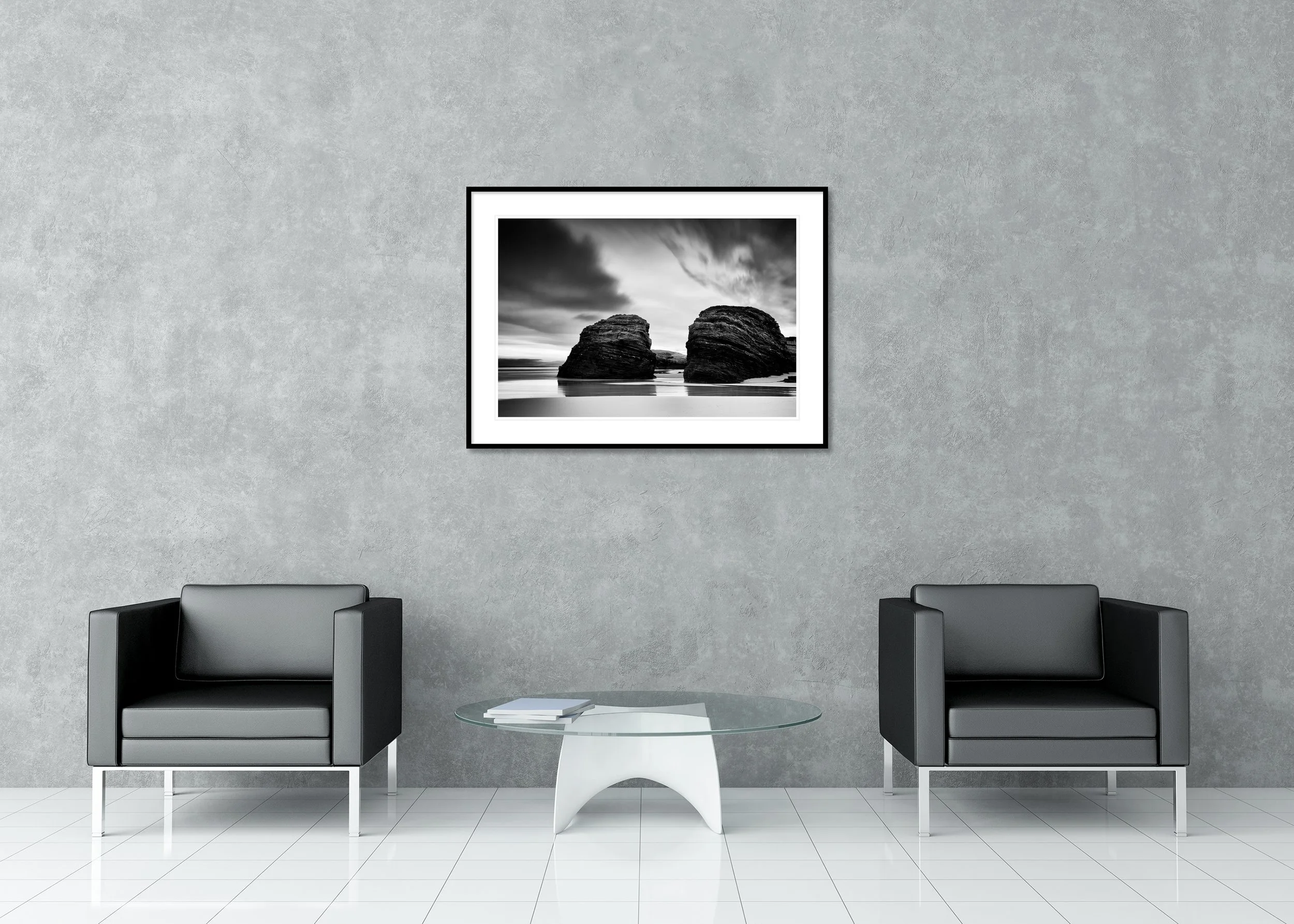 Minimalist black and white coastal landscape photo print of two large rounded rocks on the shoreline beneath a cloudy sky, archival pigment print in a classic frame with a mount.