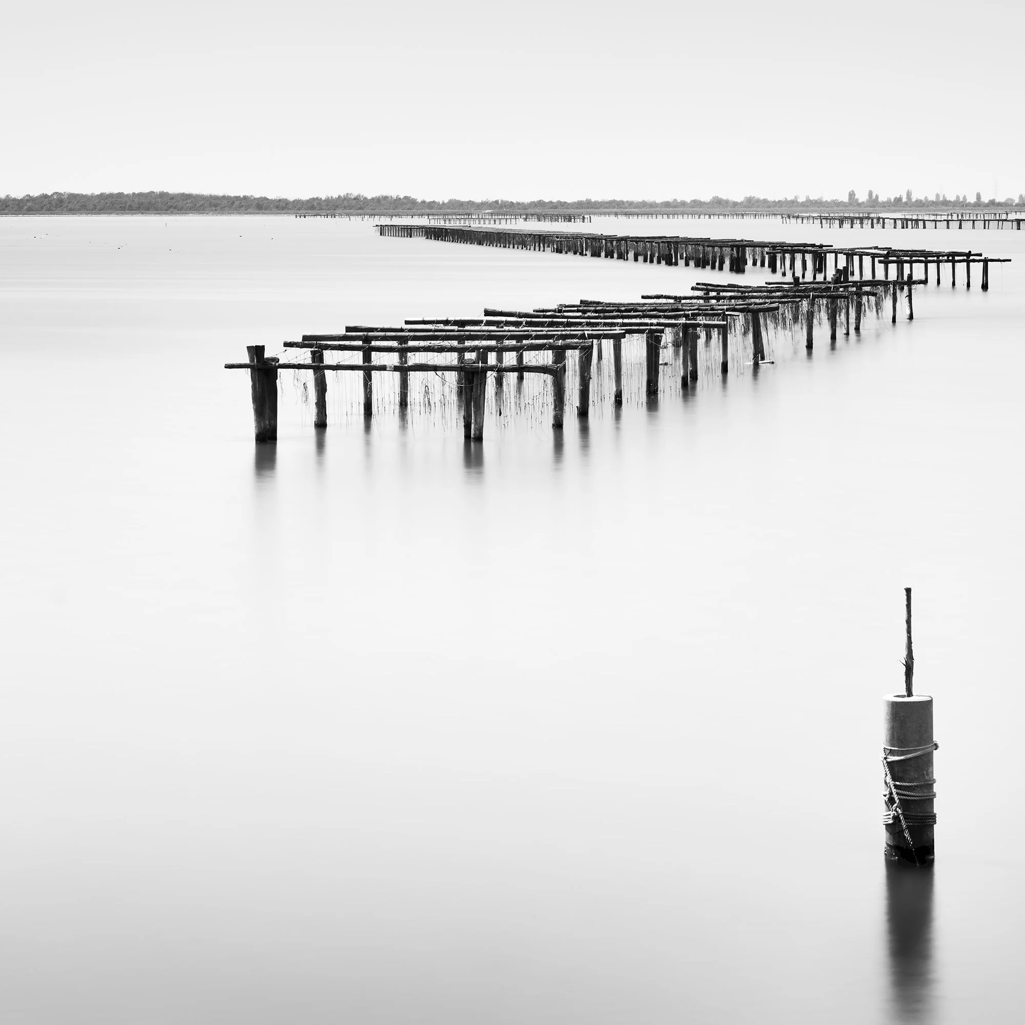 Detail of Aquaculture Structures Study 4 showing weathered wooden aquaculture structures crossing calm water in Italy by Gerald Berghammer.