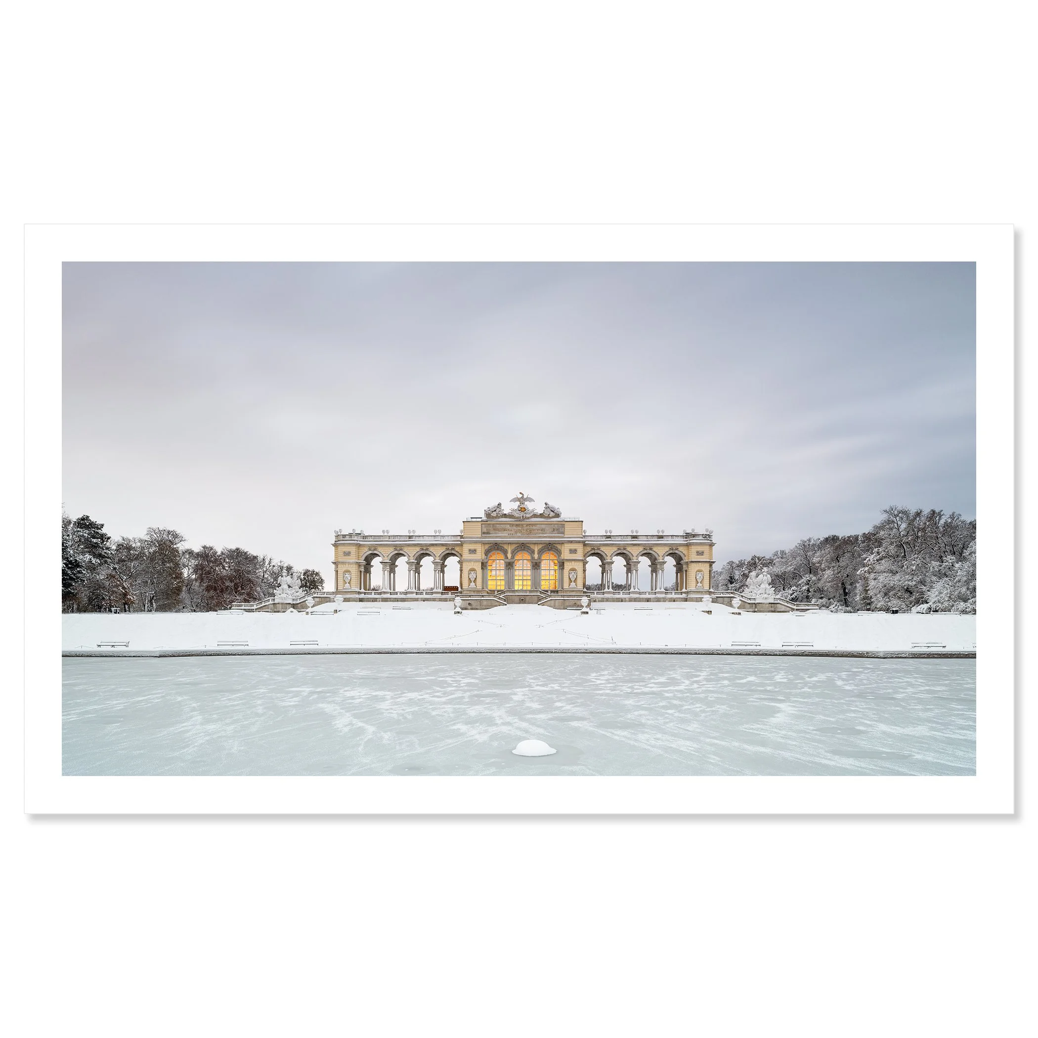Gerald Berghammer - Color Photography. A historic building on a snow-covered landscape, surrounded by leafless trees, with a frozen body of water. Fine art print only