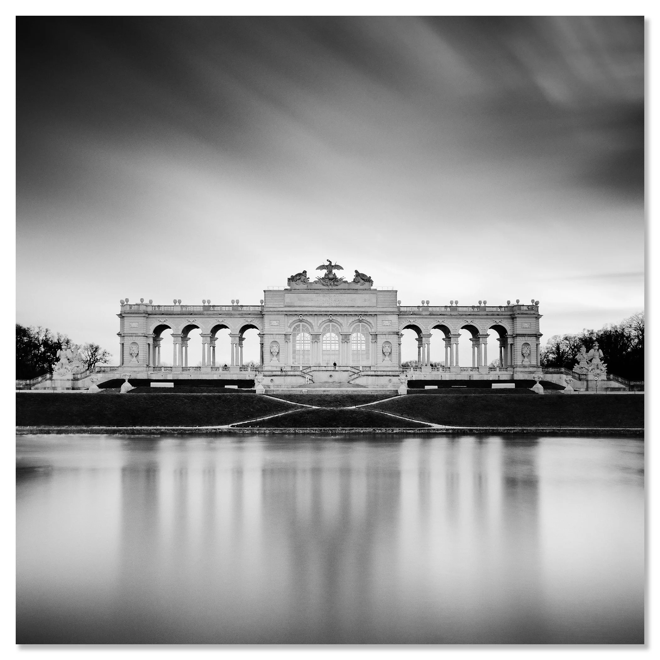 Gerald Berghammer - B&W Cityscape Photography. A large, ornate building with arches and decorative sculptures on top, reflected in a calm body of water. Chromaluxe frameless