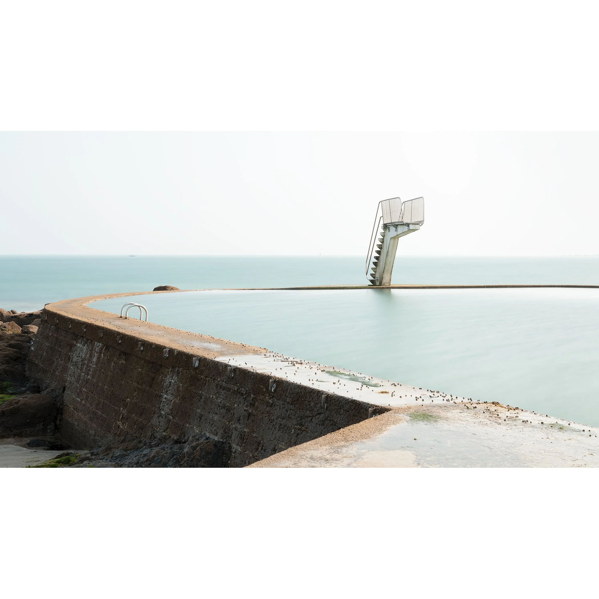 Minimalist colour photograph of a seawater swimming pool and diving platform on the French coast, photo by Gerald Berghammer.