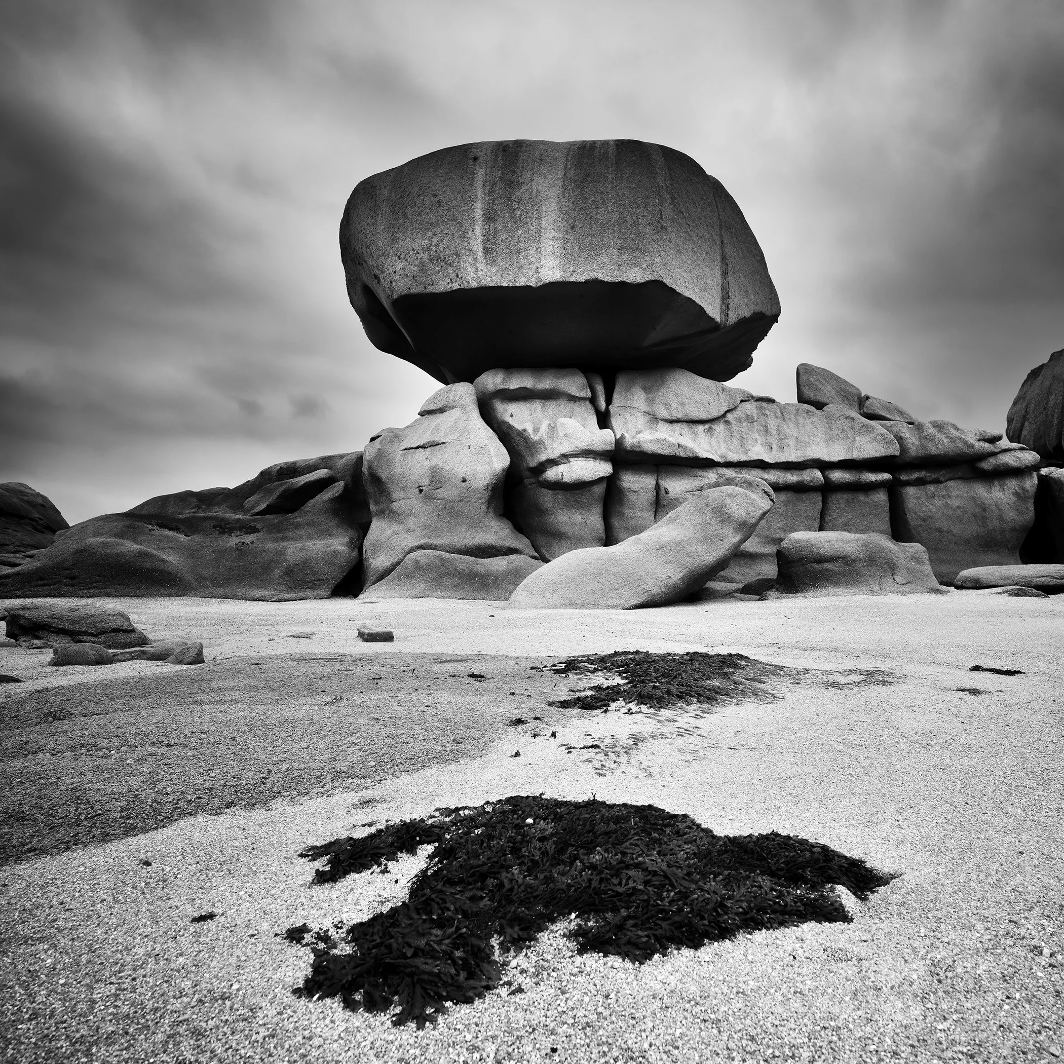 Monumental granite boulder above a rocky beach with seaweed on France’s Pink Granite Coast, photographed in black and white by Gerald Berghammer.