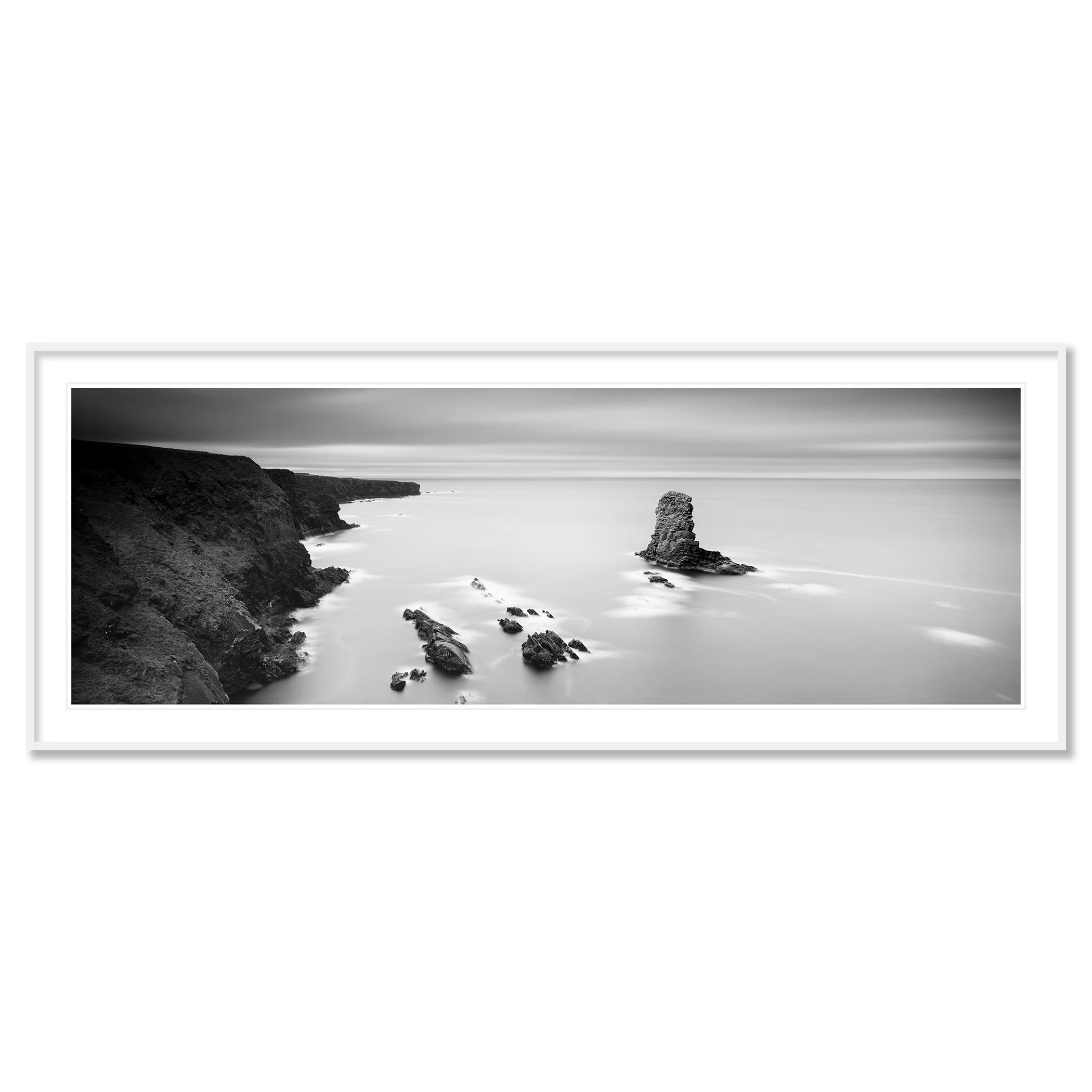 Gerald Berghammer - Black and white panorama seascape photography. Rocky coastline with cliffs and a tall rock formation in the water, under a cloudy sky. Classic framed white
