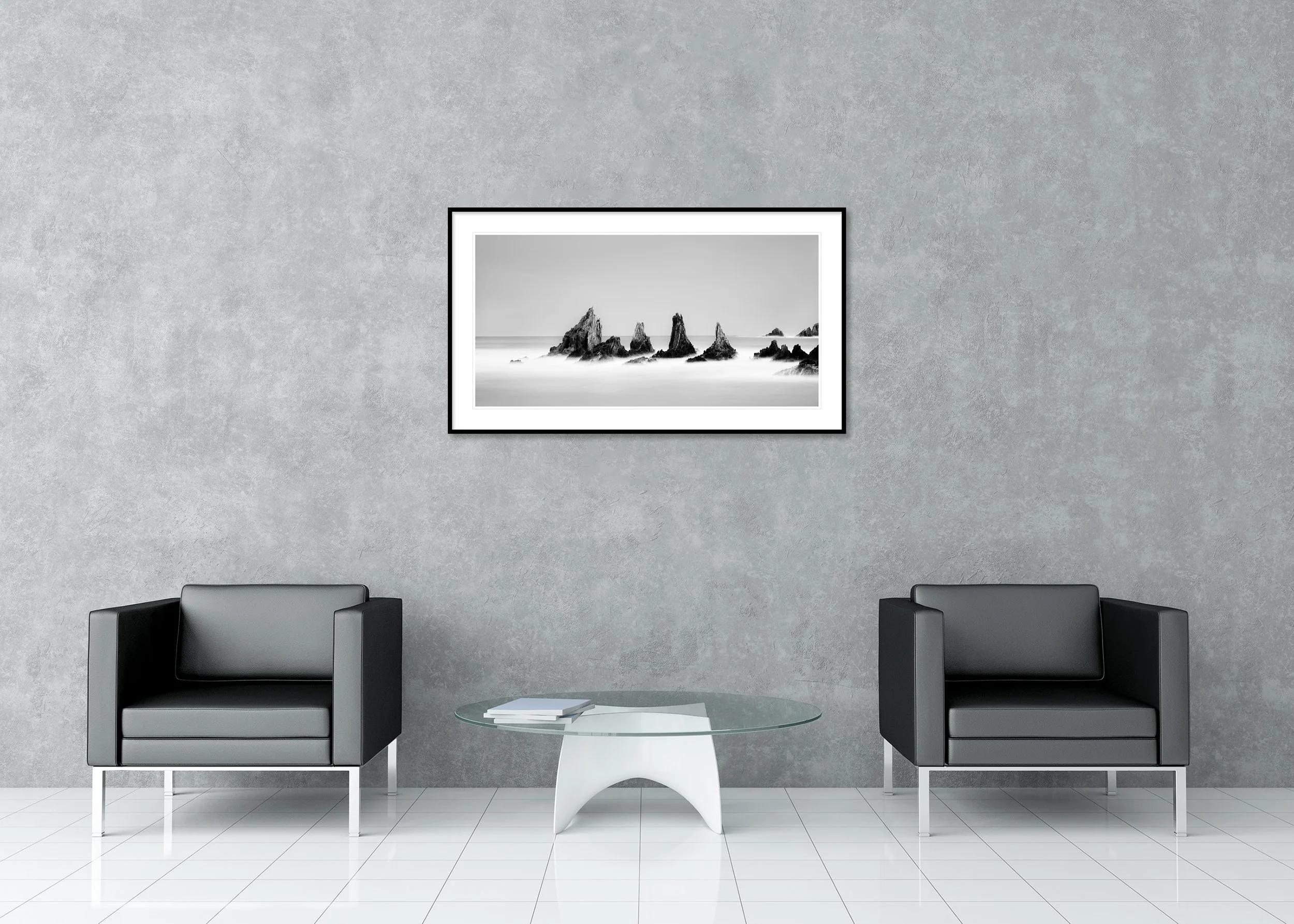 Long-exposure black-and-white ocean scene with jagged rocks, misty water and clear sky, archival pigment print in a classic frame with a mount.