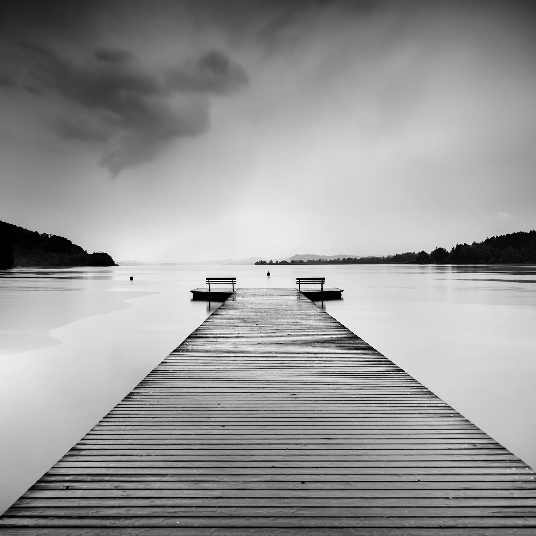 Black and white landscape photo of a wooden jetty at Lake Wallersee, Austria, with a clean horizon.